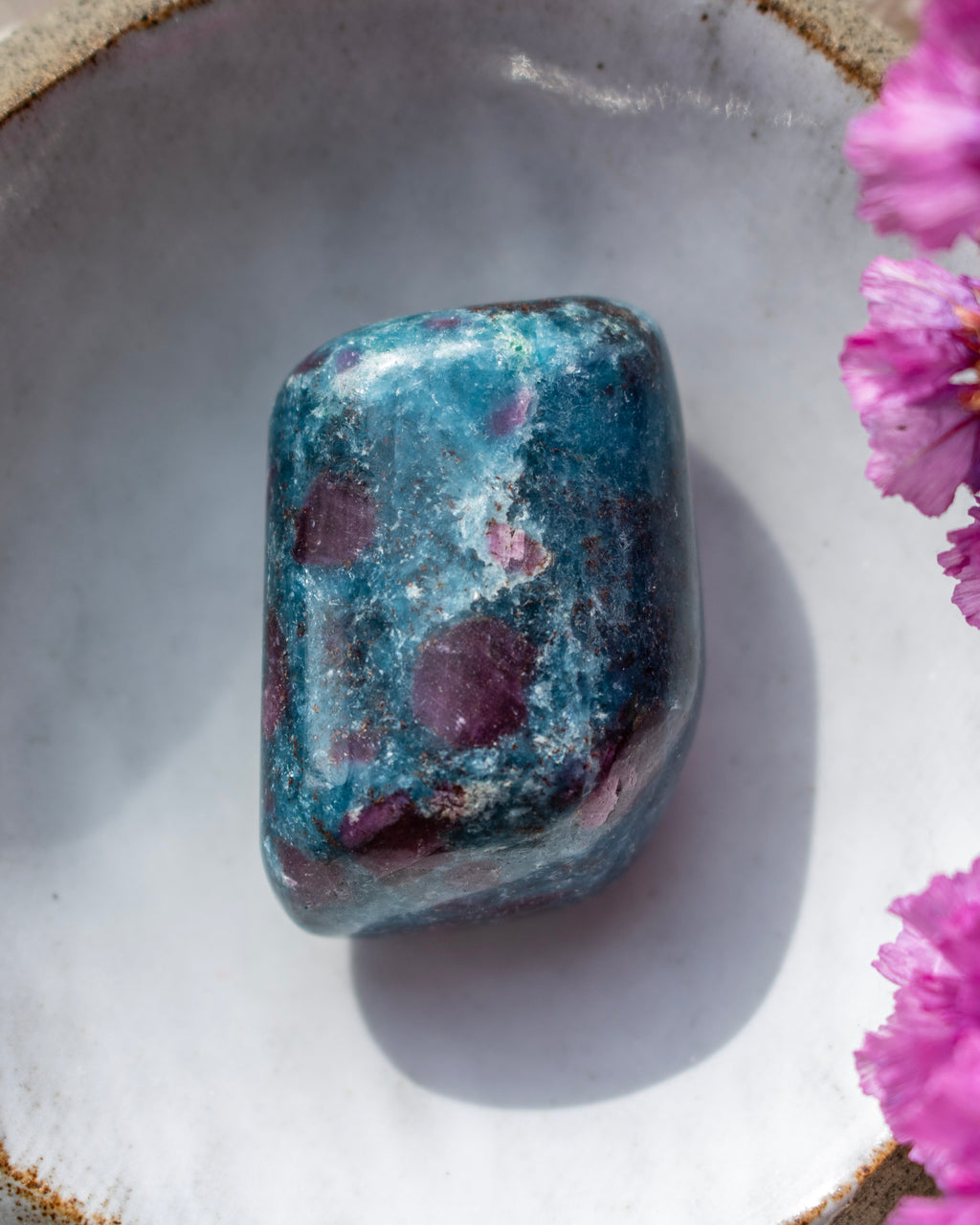 a dark blue and purple stone in a ceramic dish with purple flowers