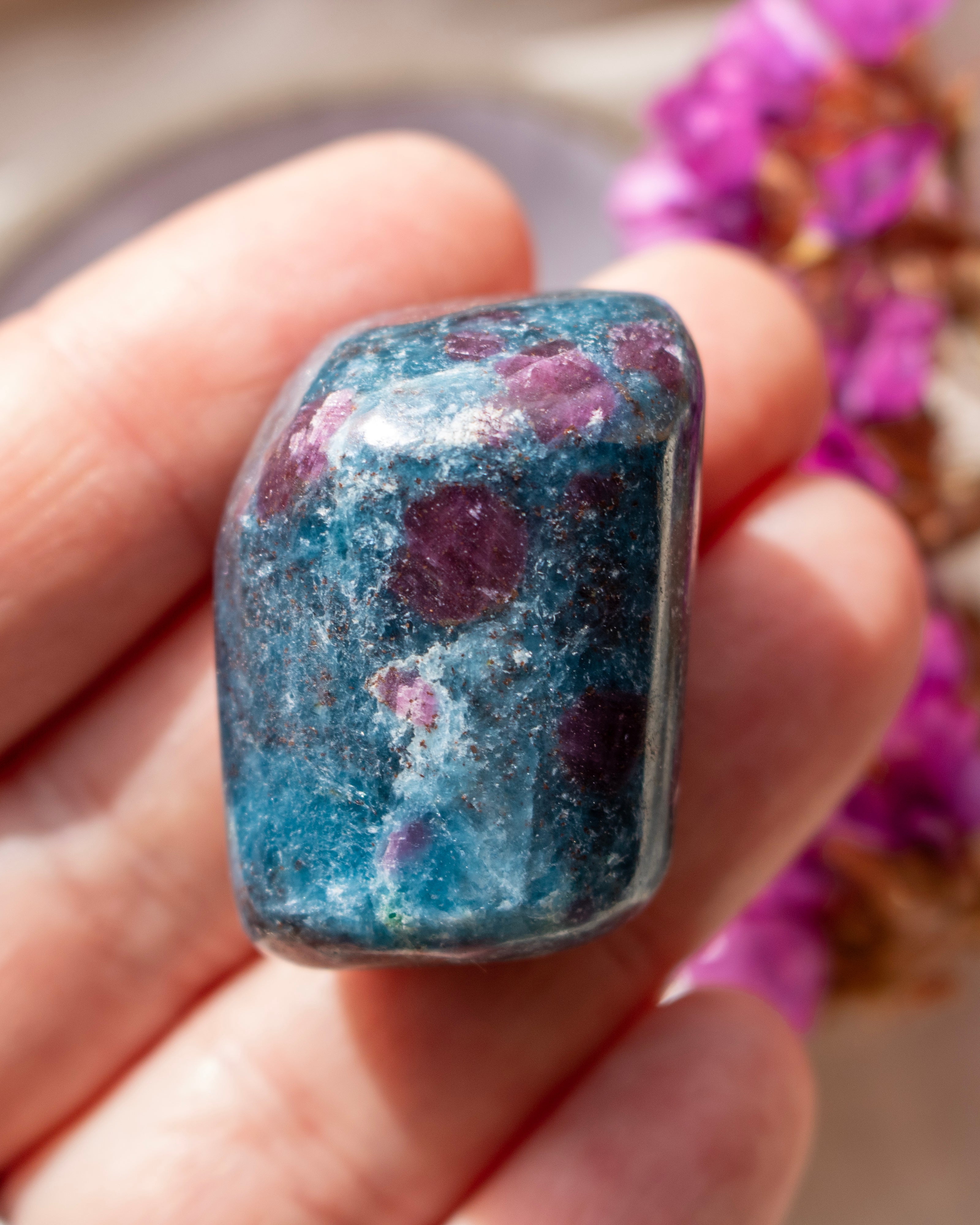 a dark blue and purple stone being held on fingers with a blurred background