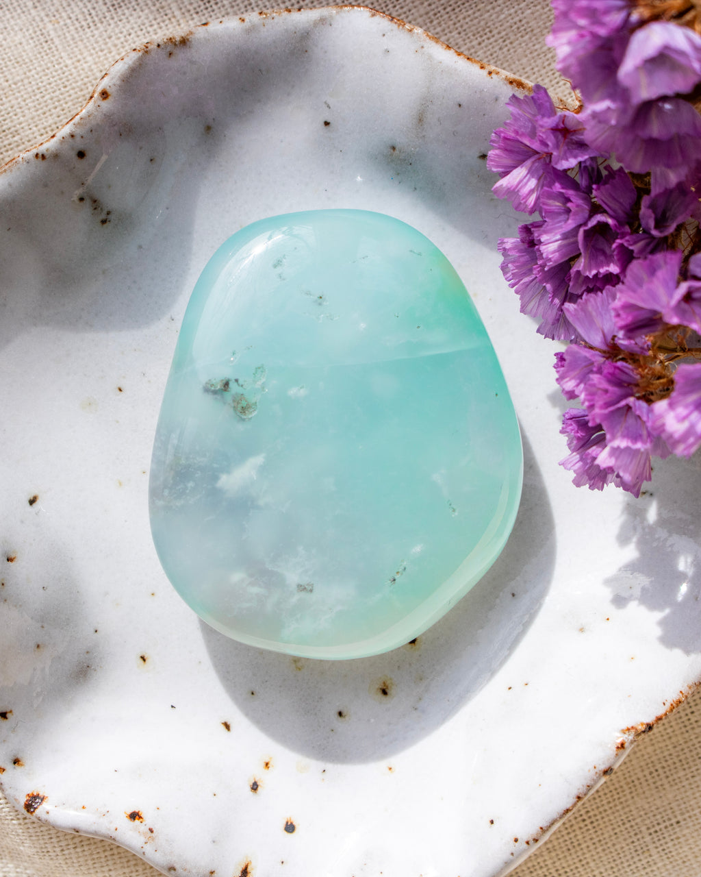 a soft blue stone with rounded edges in a white ceramic dish with purple flowers