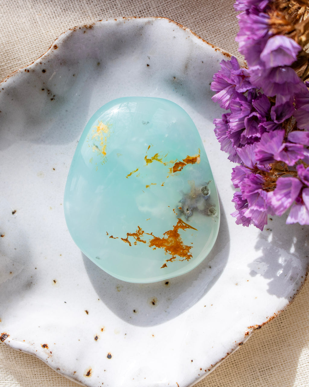 a soft blue stone with rounded edges in a white ceramic dish with purple flowers