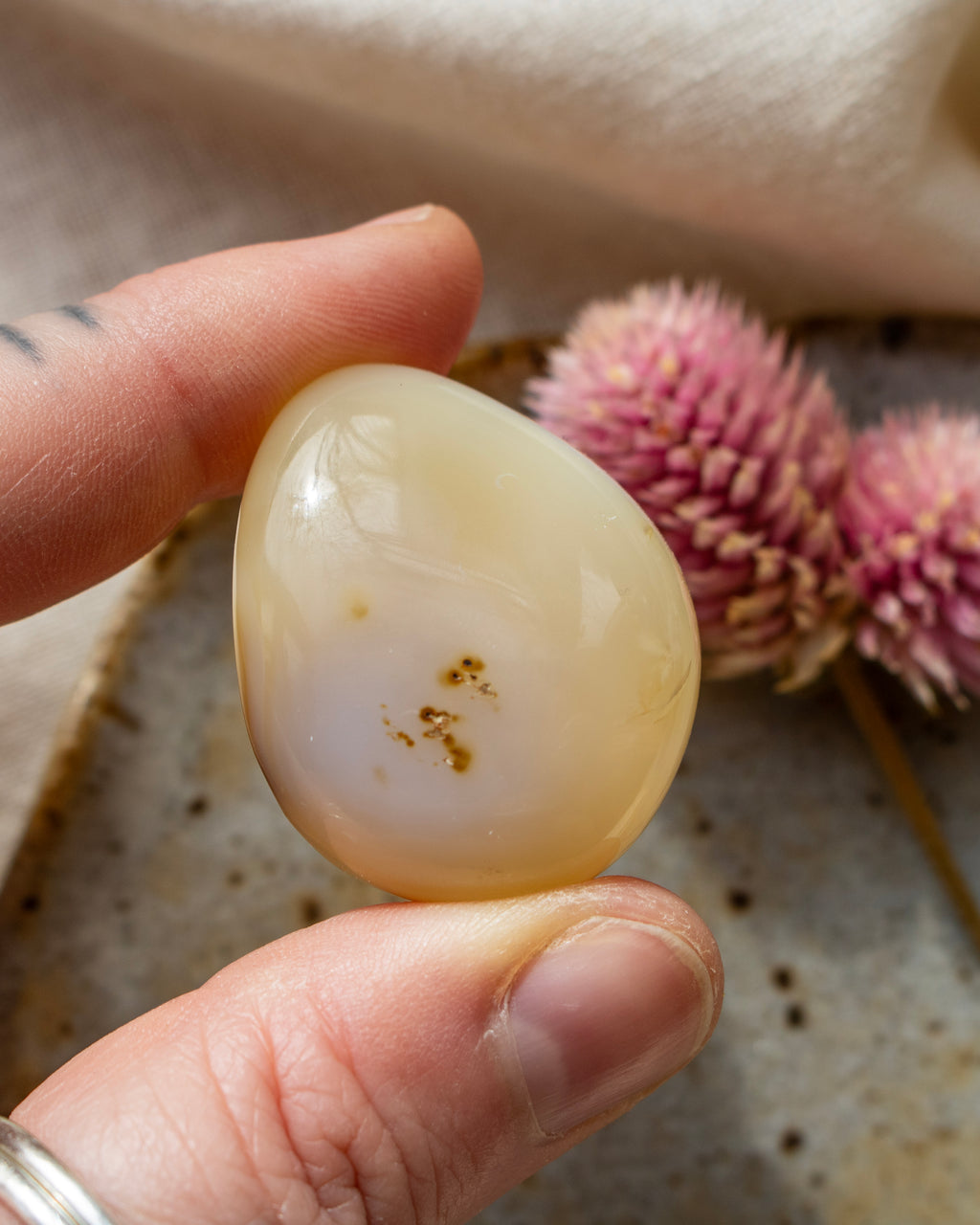 a yellowy beige pebble being held with fingers and a blurred background