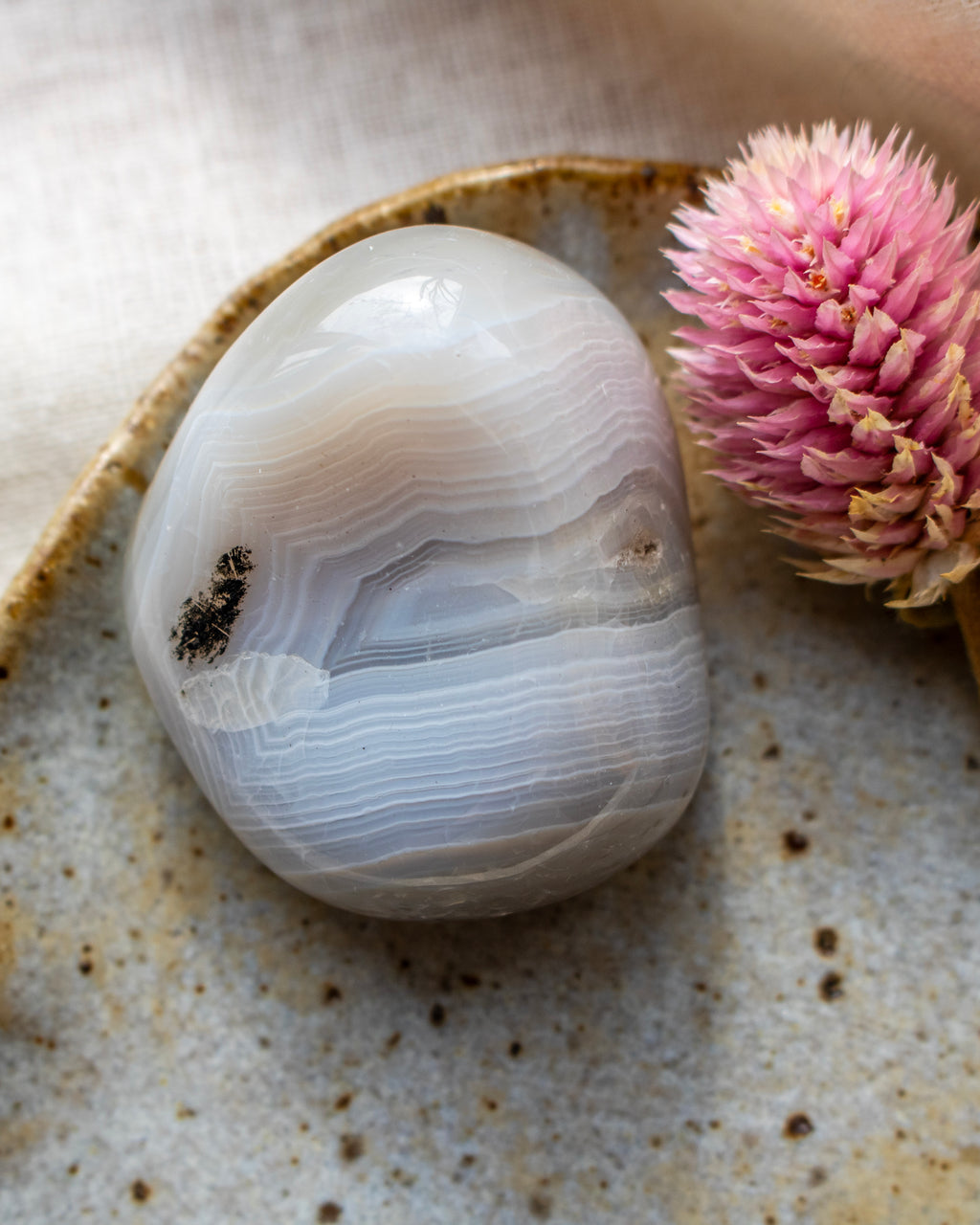 a banded agate pebble on a brown ceramic dish with a pink flower