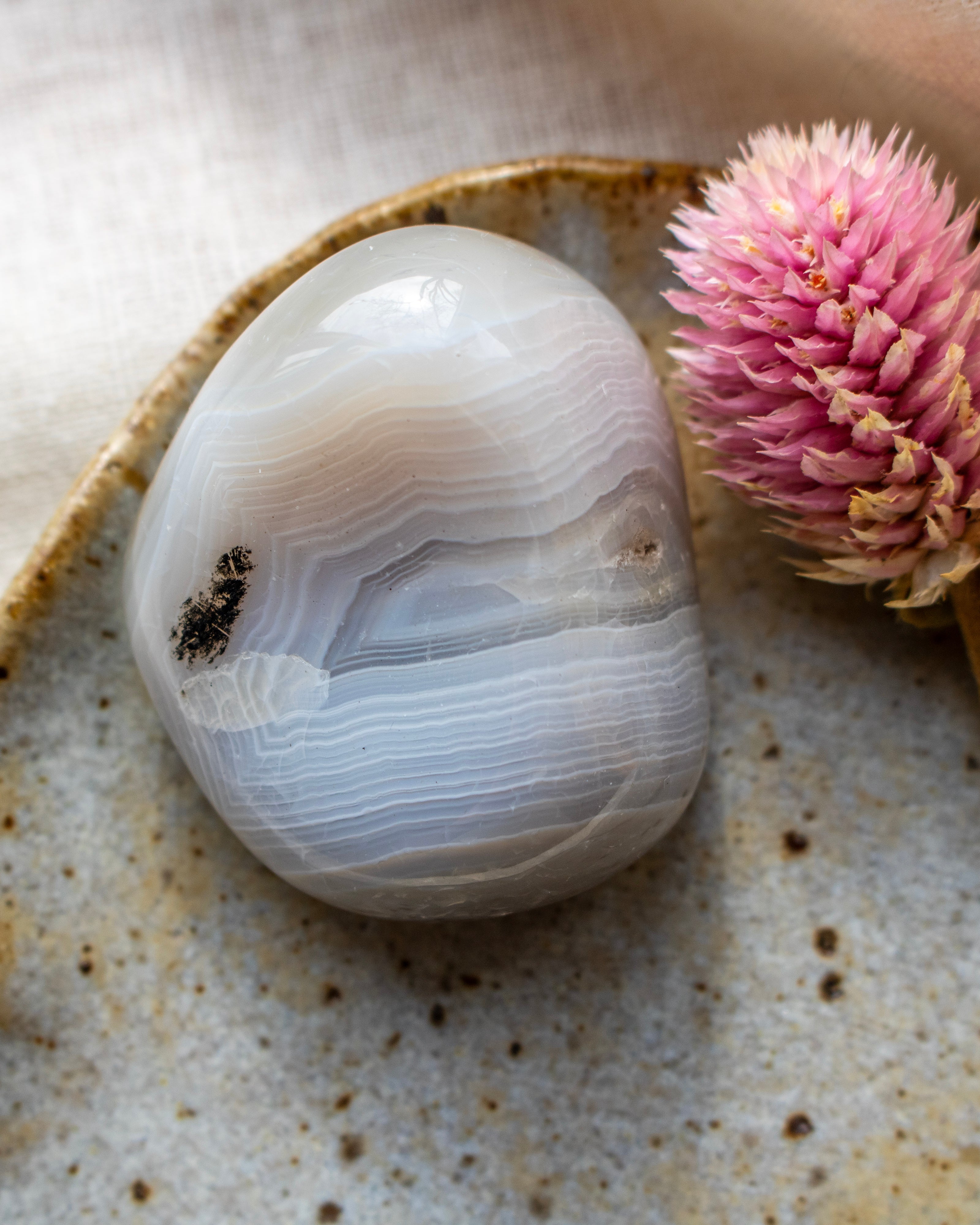 a banded agate pebble on a brown ceramic dish with a pink flower