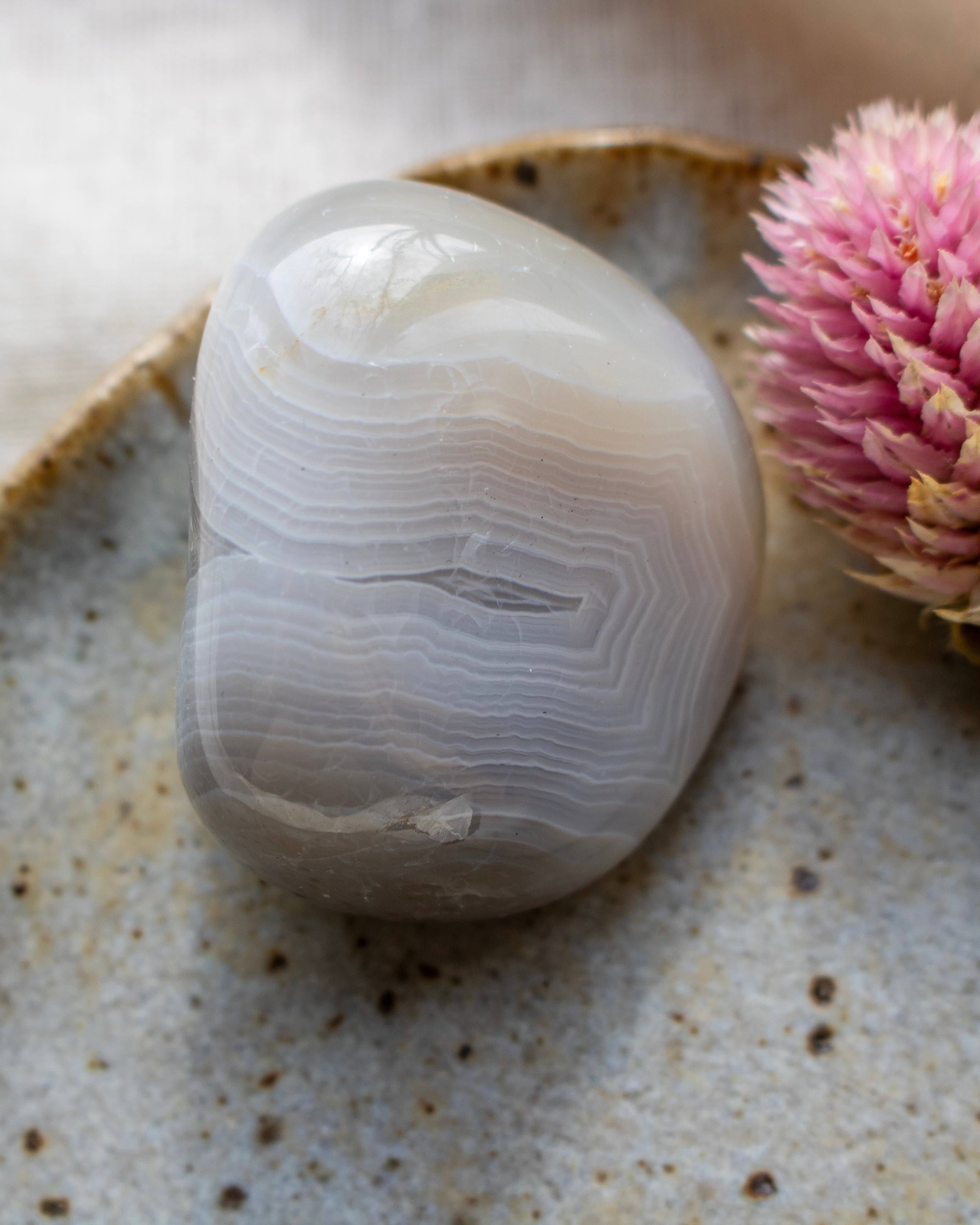 a banded agate pebble on a brown ceramic dish with a pink flower
