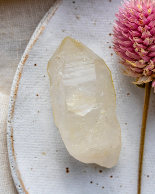 a quartz point on a white ceramic dish with a pink flower