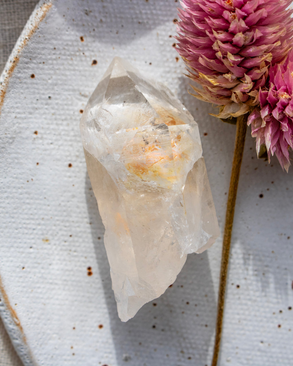 a quartz point crystal on a white plate with a pink flower