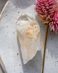 a quartz point crystal on a white plate with a pink flower