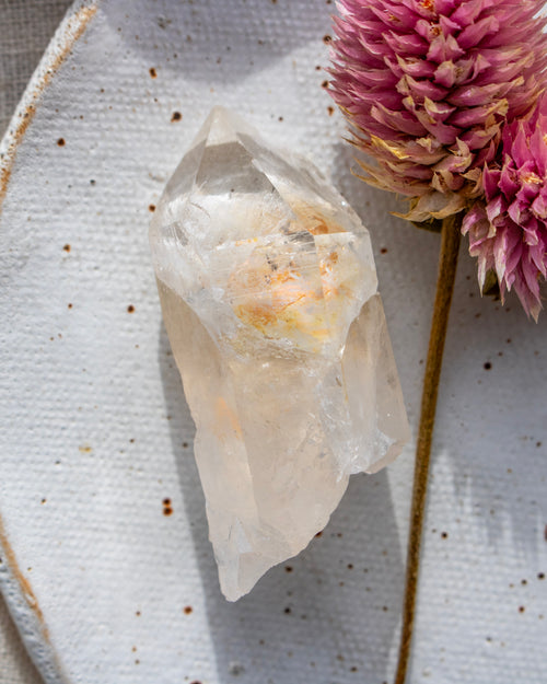 a quartz point crystal on a white plate with a pink flower