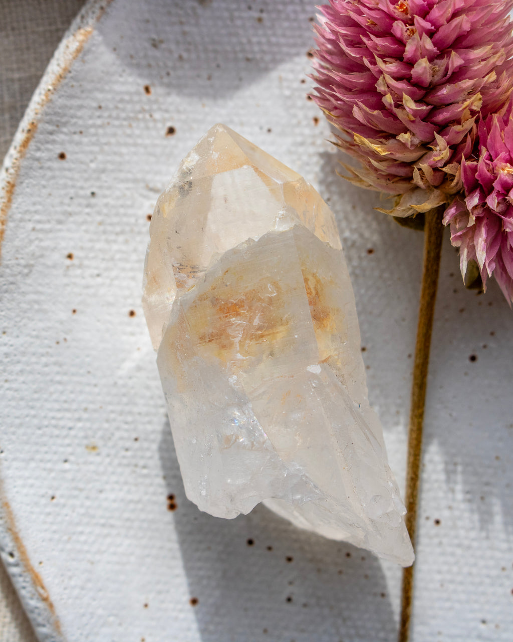 a quartz point crystal on a white plate with a pink flower
