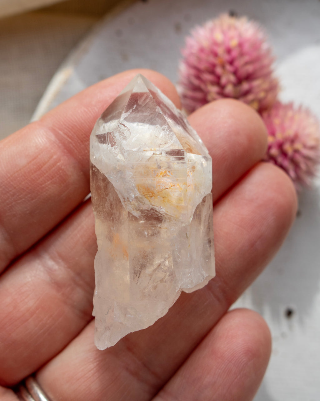 a quartz point crystal on a white plate with a pink flower