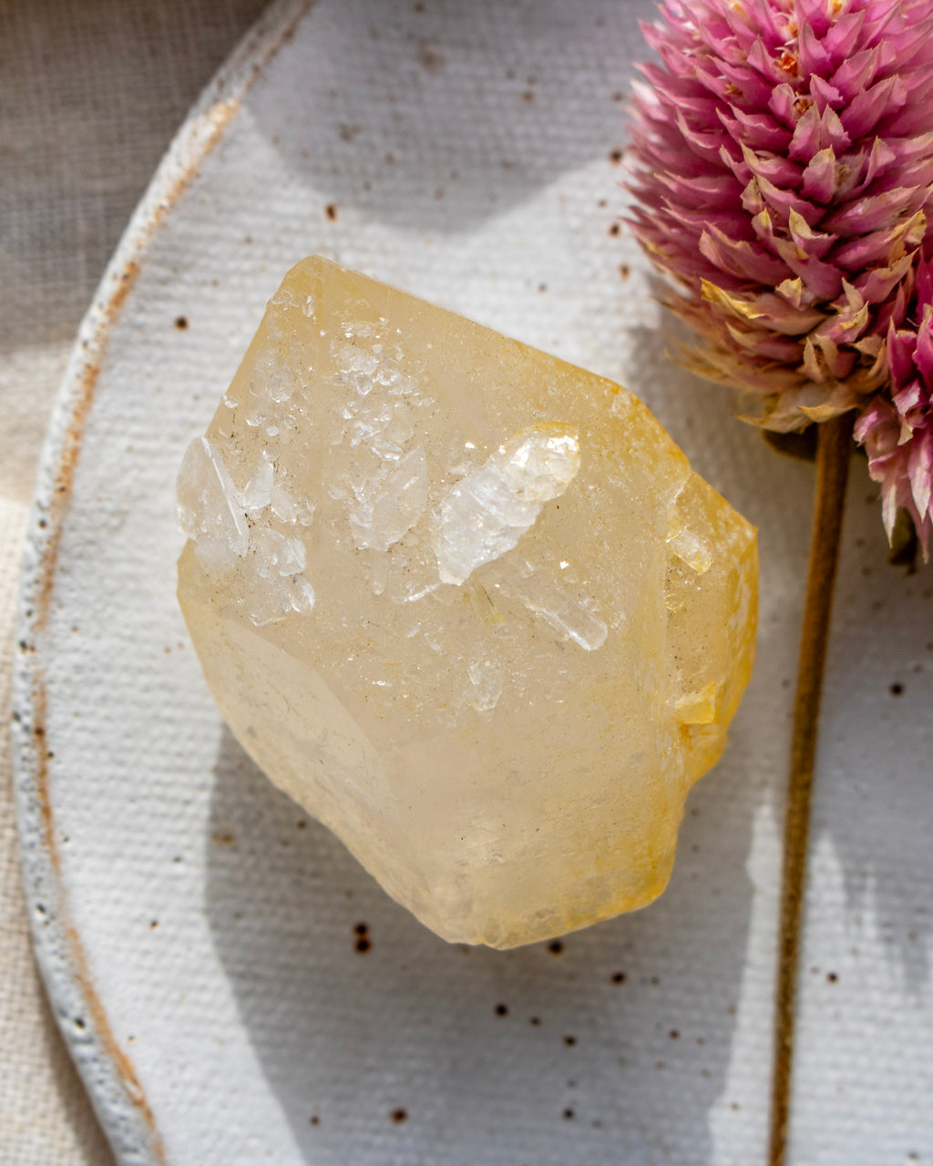 a yellow quartz crystal on a ceramic dish with a pink flower