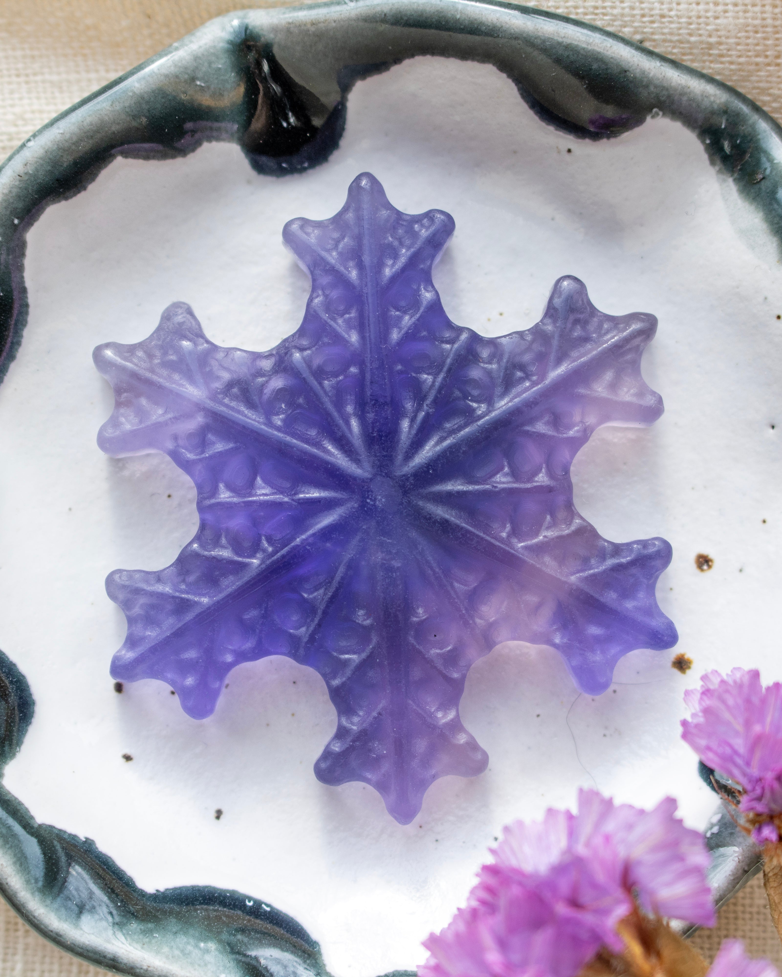 Purple snowflake-shaped object on a white surface with pink flowers in the background