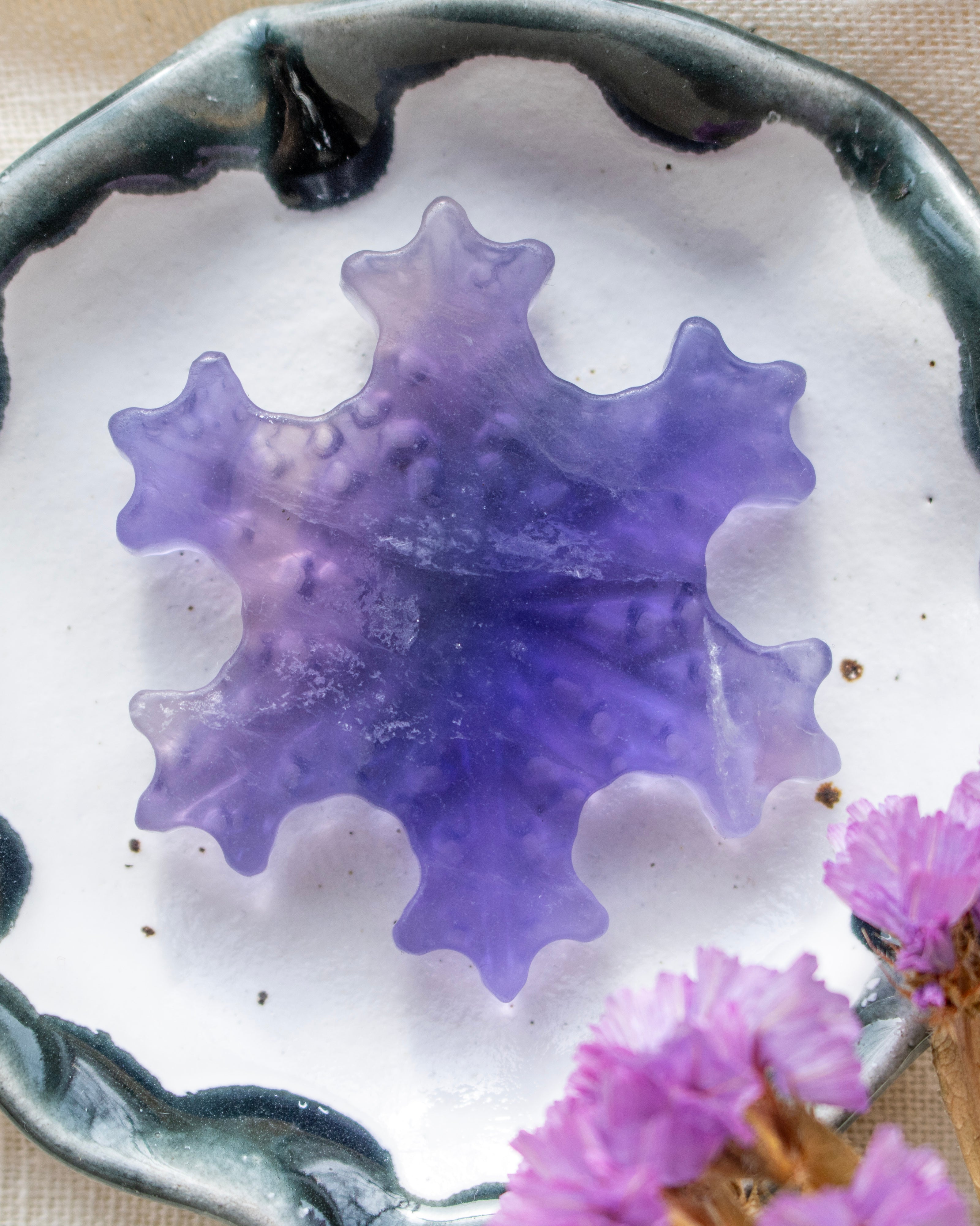 Purple decorative stone on a white surface with pink flowers in the background
