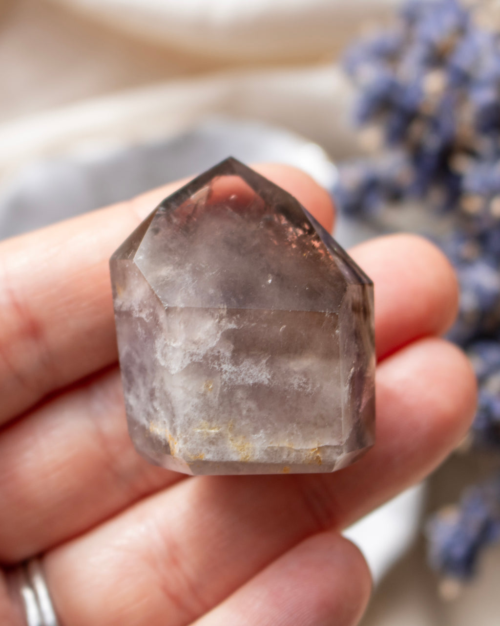 Clear crystal held in a hand with blurred lavender flowers in the background