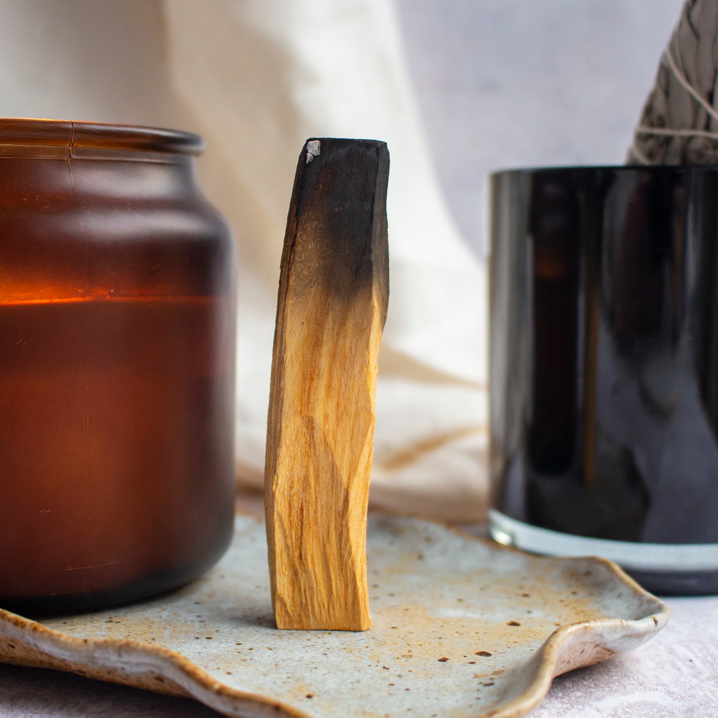 A single Palo Santo stick standing upright between two unlit candle jars, creating a serene and balanced display.