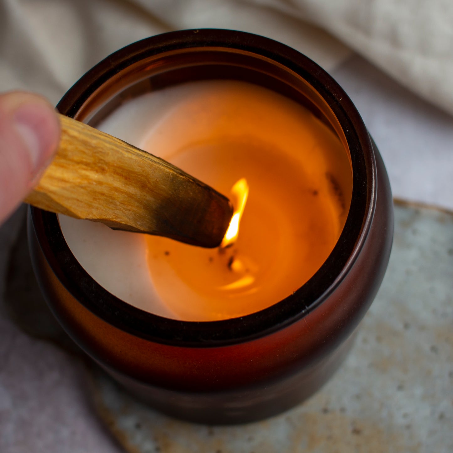 A Palo Santo stick being lit by the flame of a candle, ready to release its aromatic smoke.