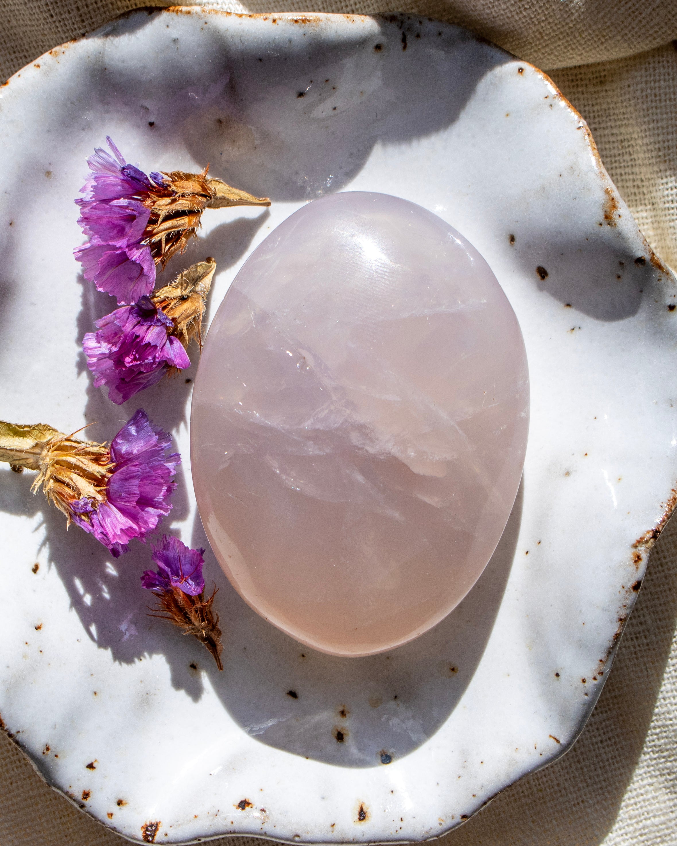 Pink crystal oval on a textured white surface with dried purple flowers