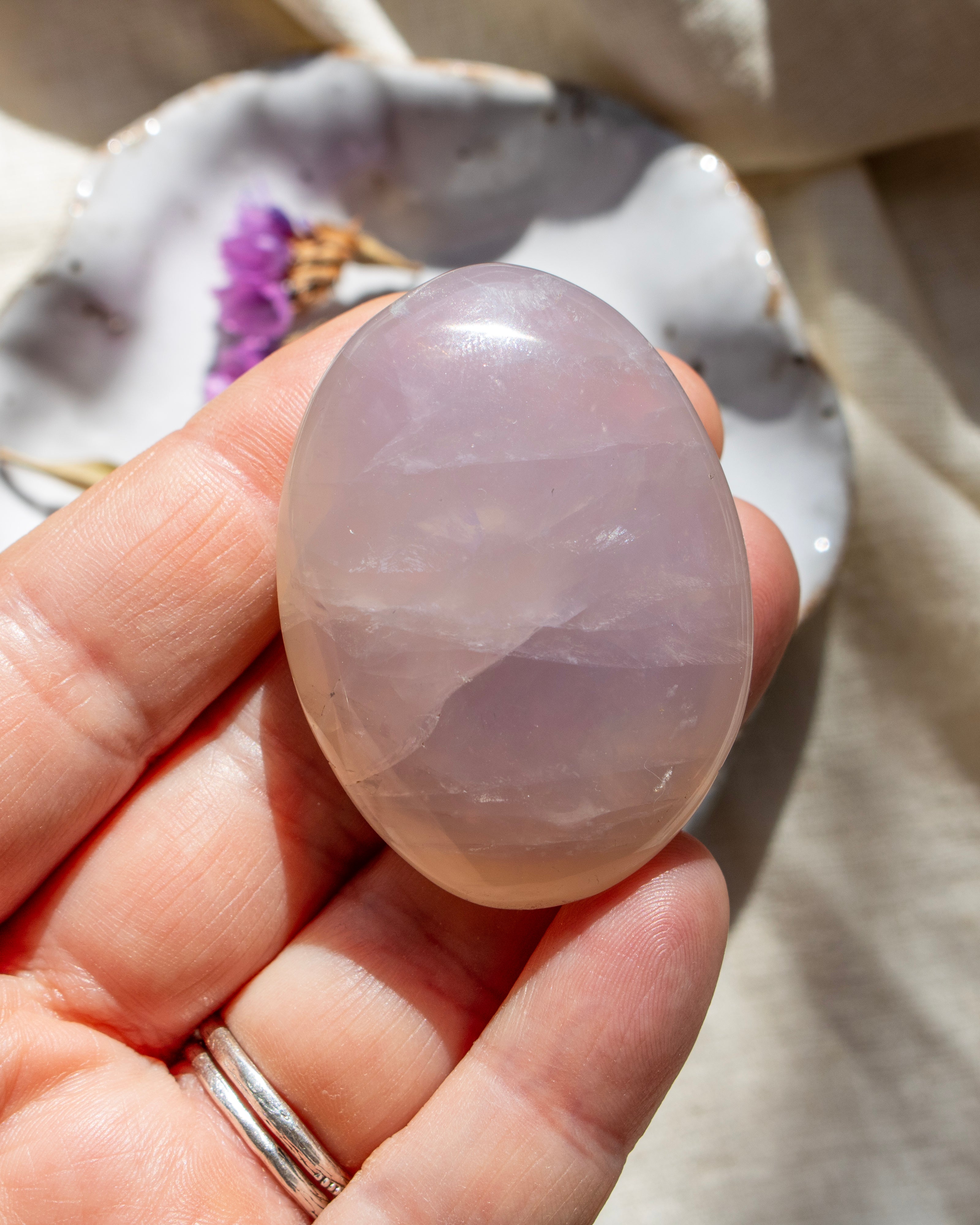 Hand holding a pink crystal stone with a blurred natural background