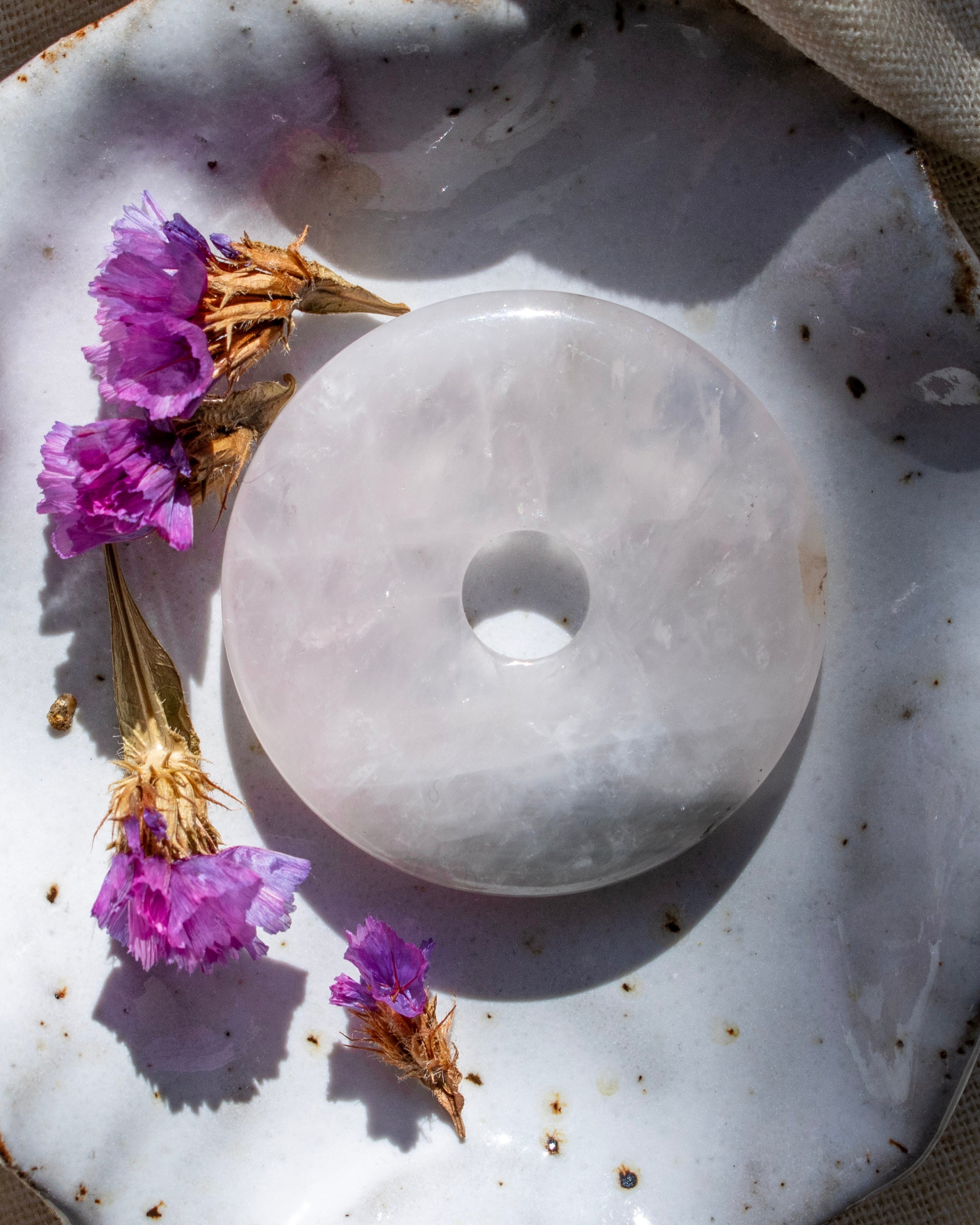 White stone disc on a textured surface with purple flowers