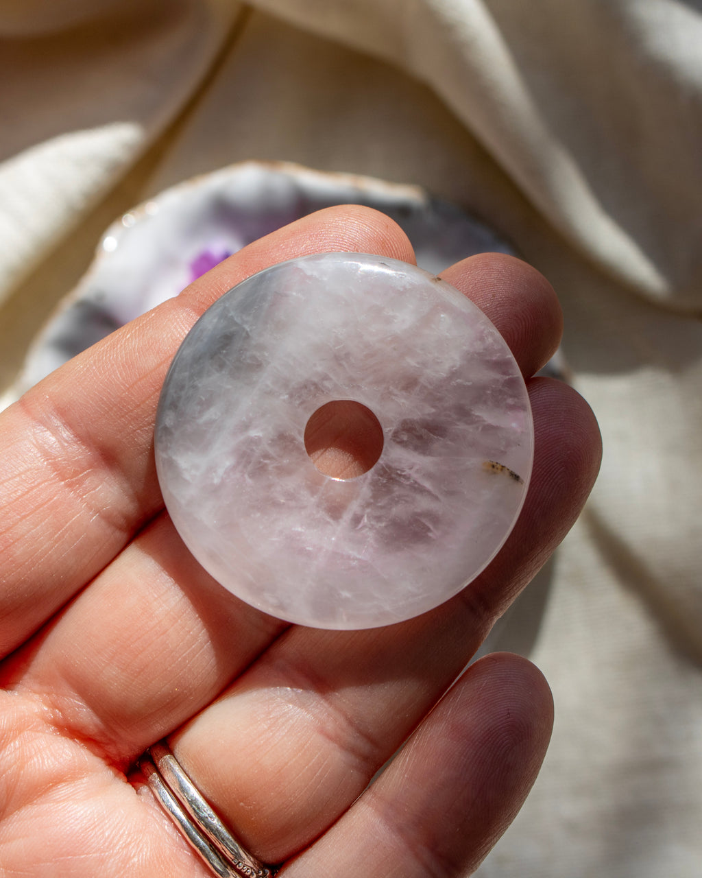 Hand holding a pink crystal disc against a neutral background