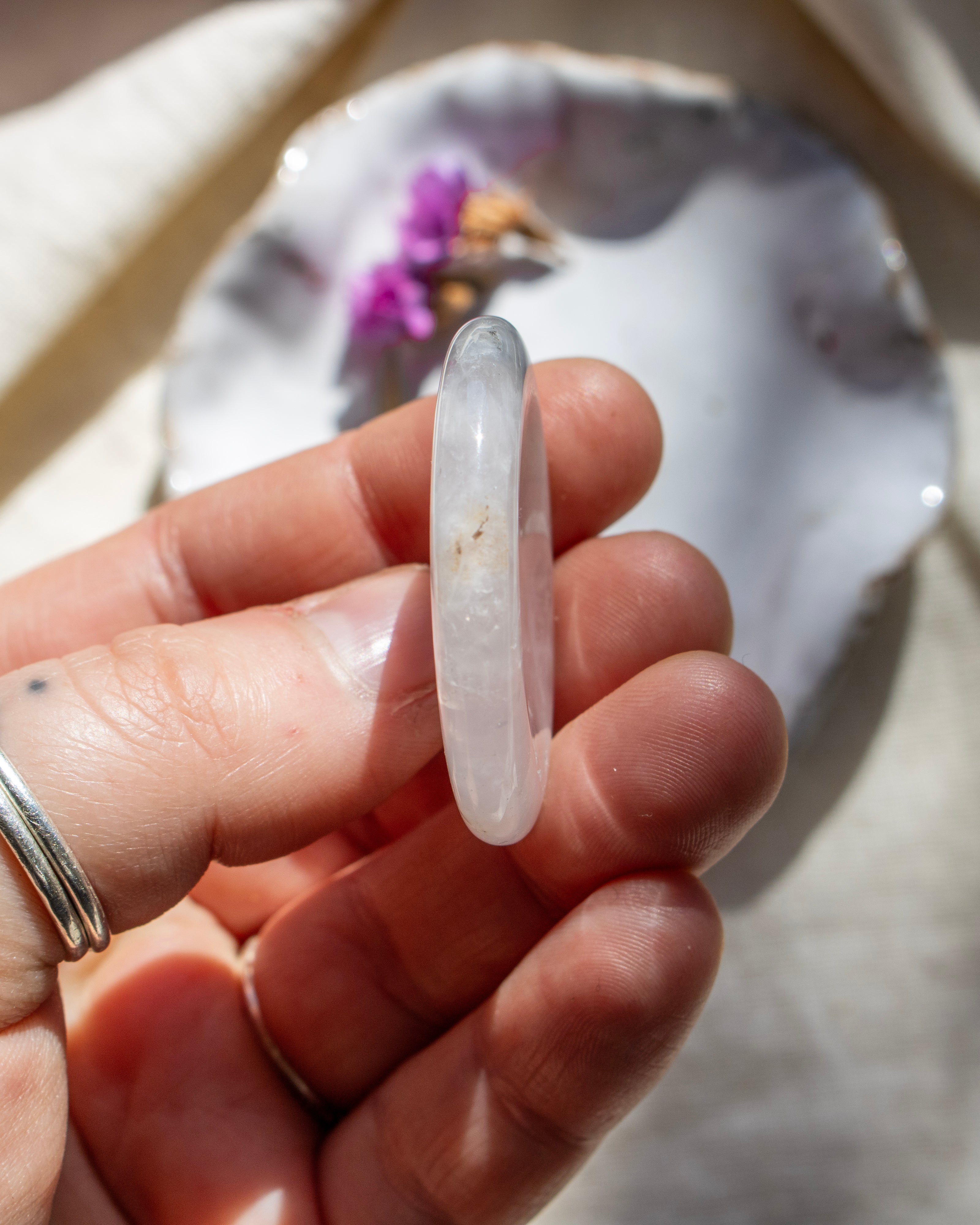 Hand holding a clear crystal with a blurred shell and flowers in the background