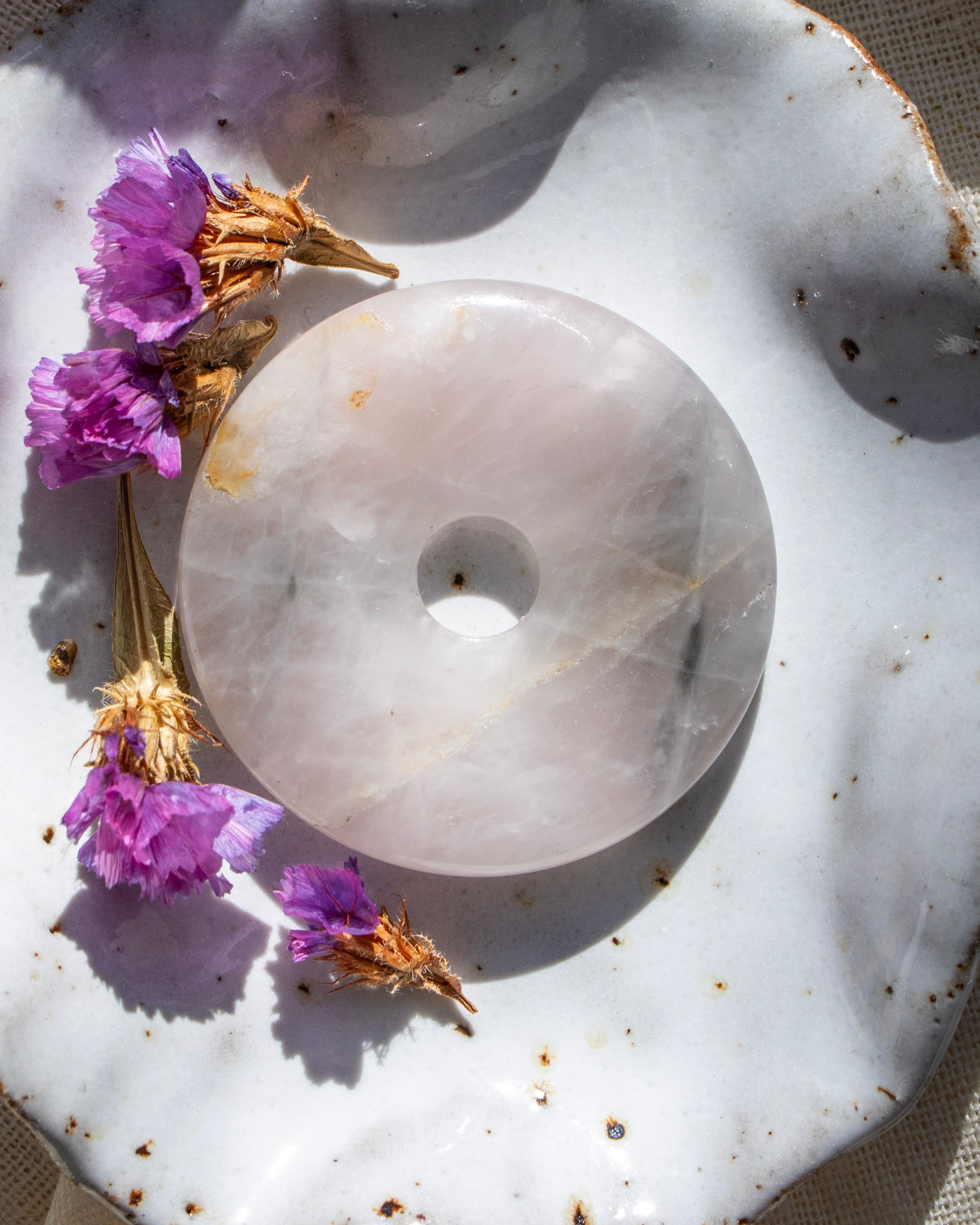 White stone disc with a central hole on a textured surface with purple flowers.
