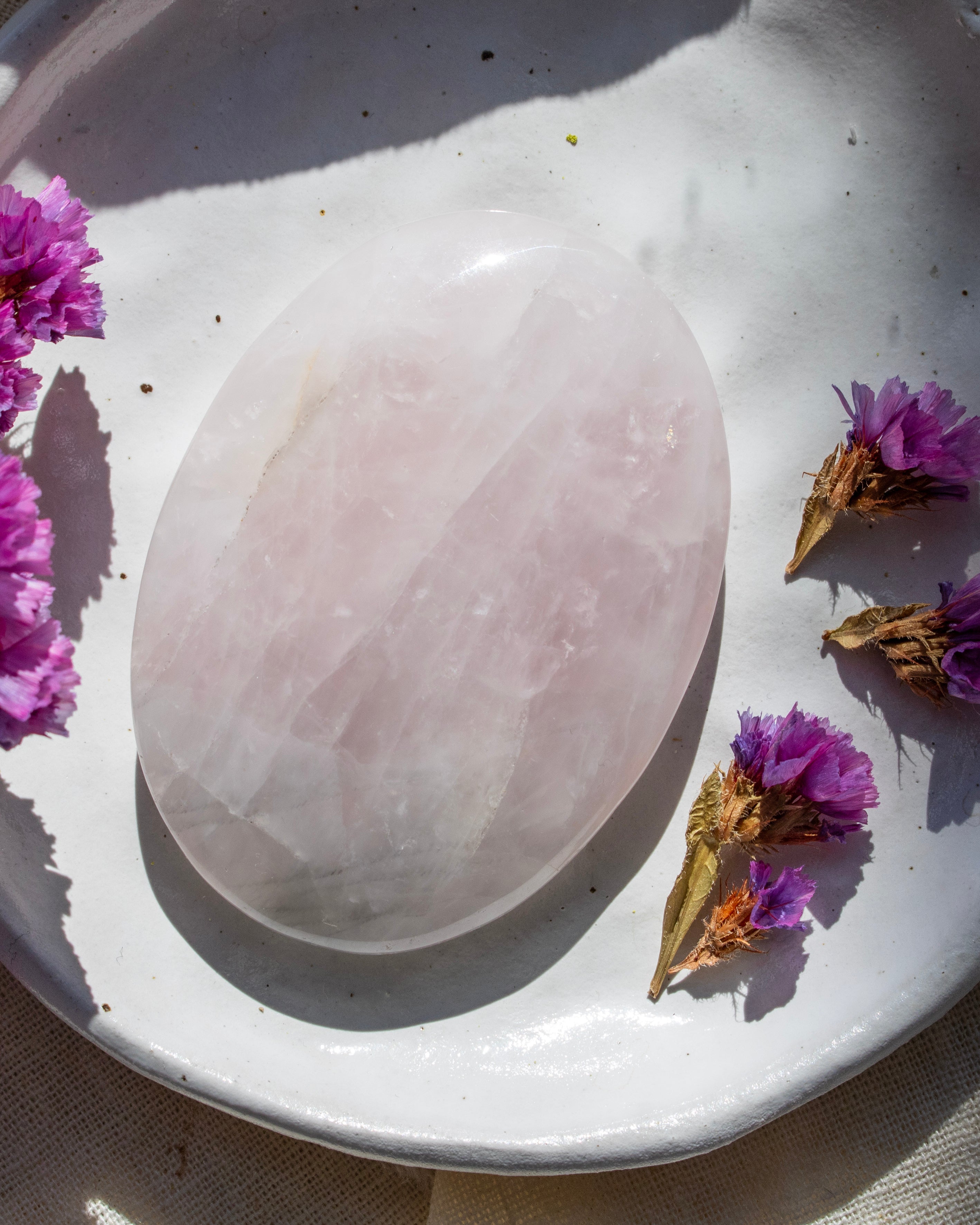 Rose quartz stone on a white plate with purple flowers