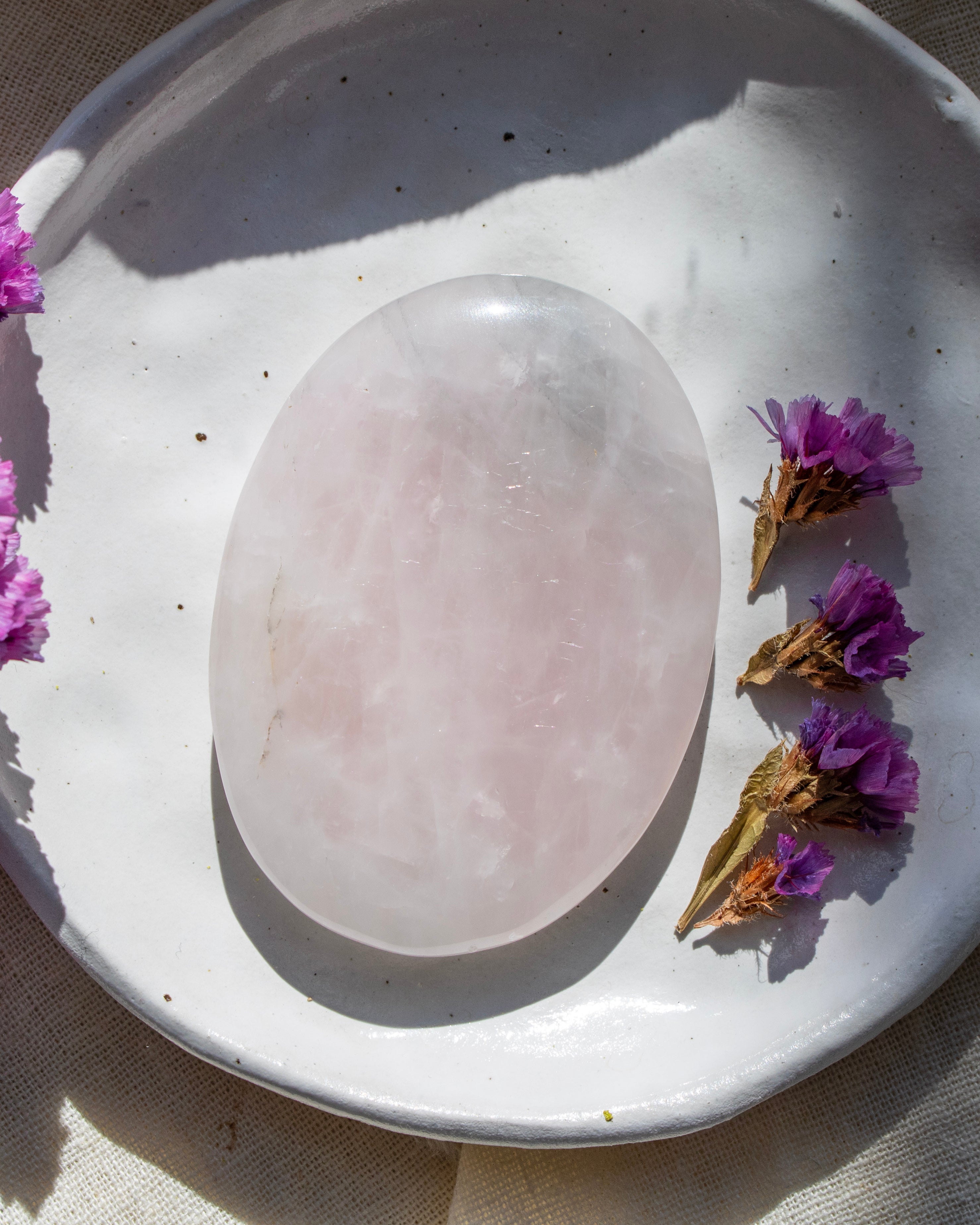 Rose quartz crystal on a white plate with purple flowers