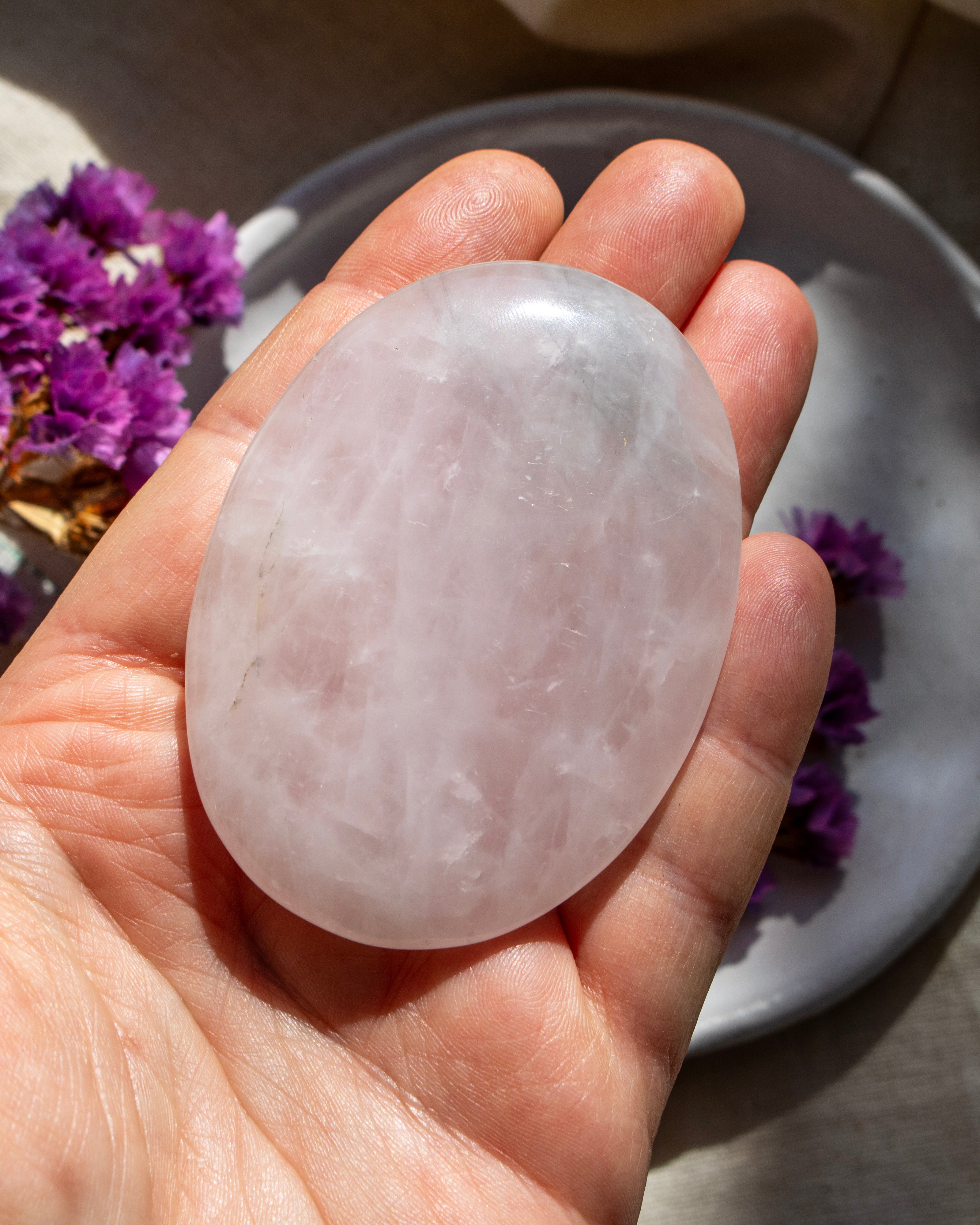 Hand holding a pink crystal stone with purple flowers in the background