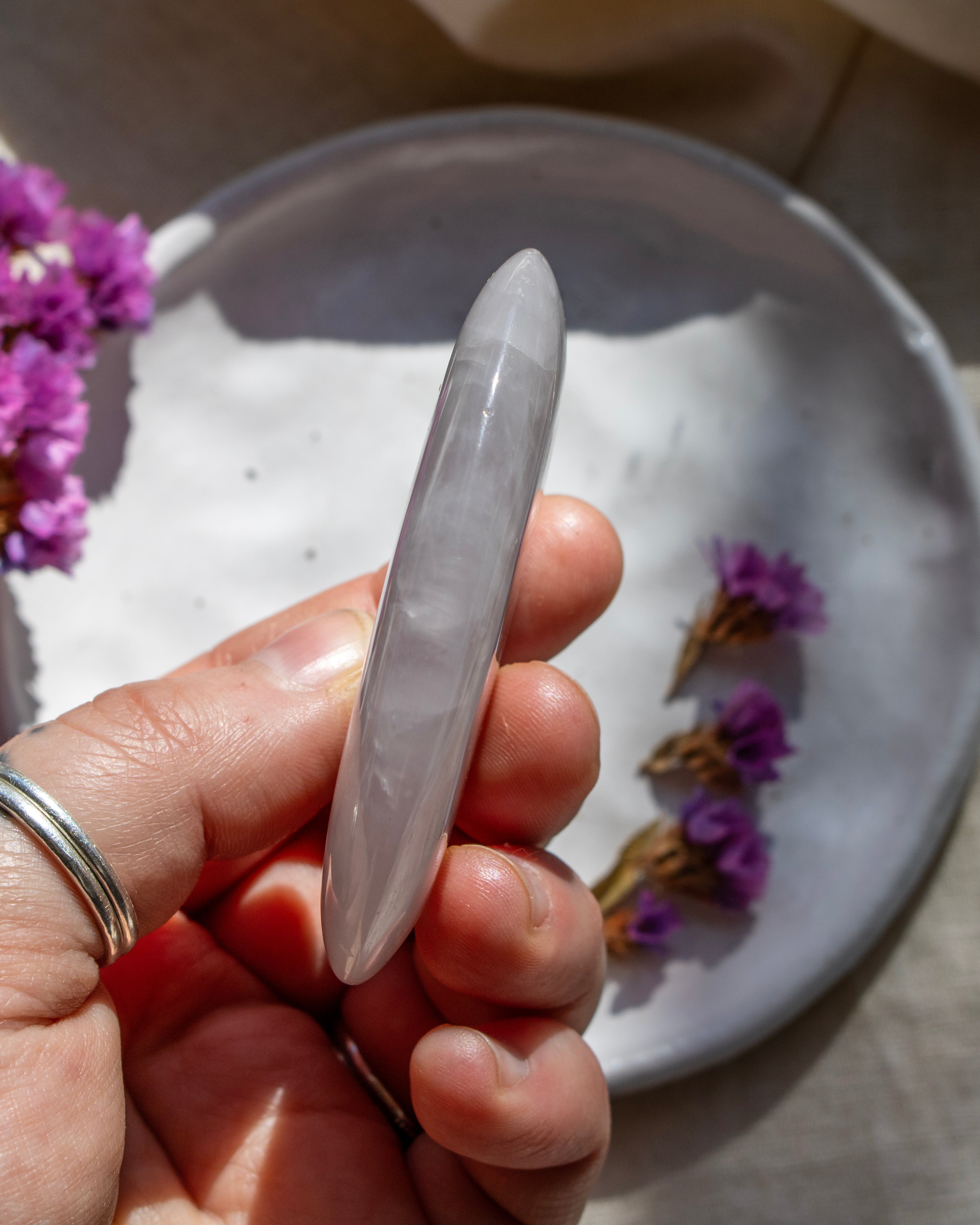 Hand holding a clear crystal object with purple flowers on a white plate in the background