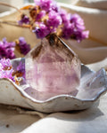 Amethyst crystal on a decorative plate with purple flowers in the background