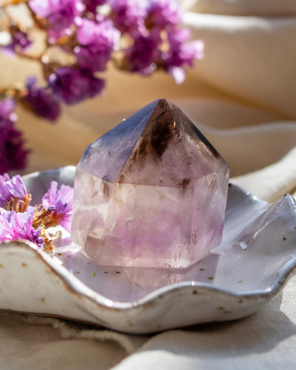 Amethyst crystal on a decorative plate with purple flowers in the background