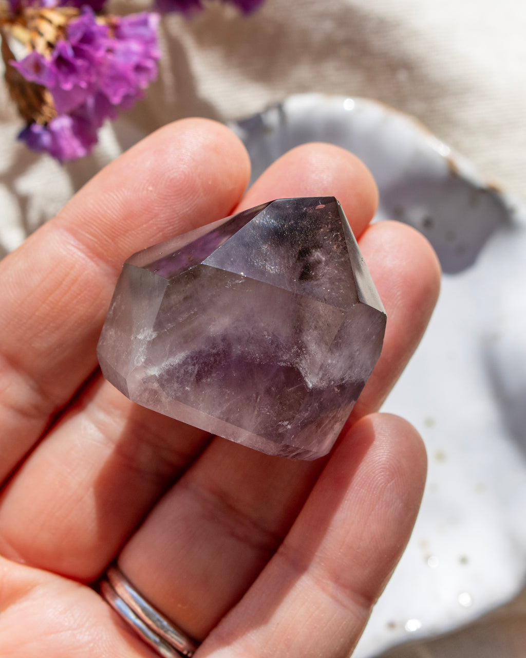 Hand holding a clear crystal with purple hues, blurred natural background