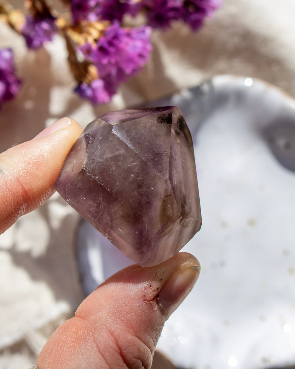 Hand holding a purple crystal with blurred flowers in the background