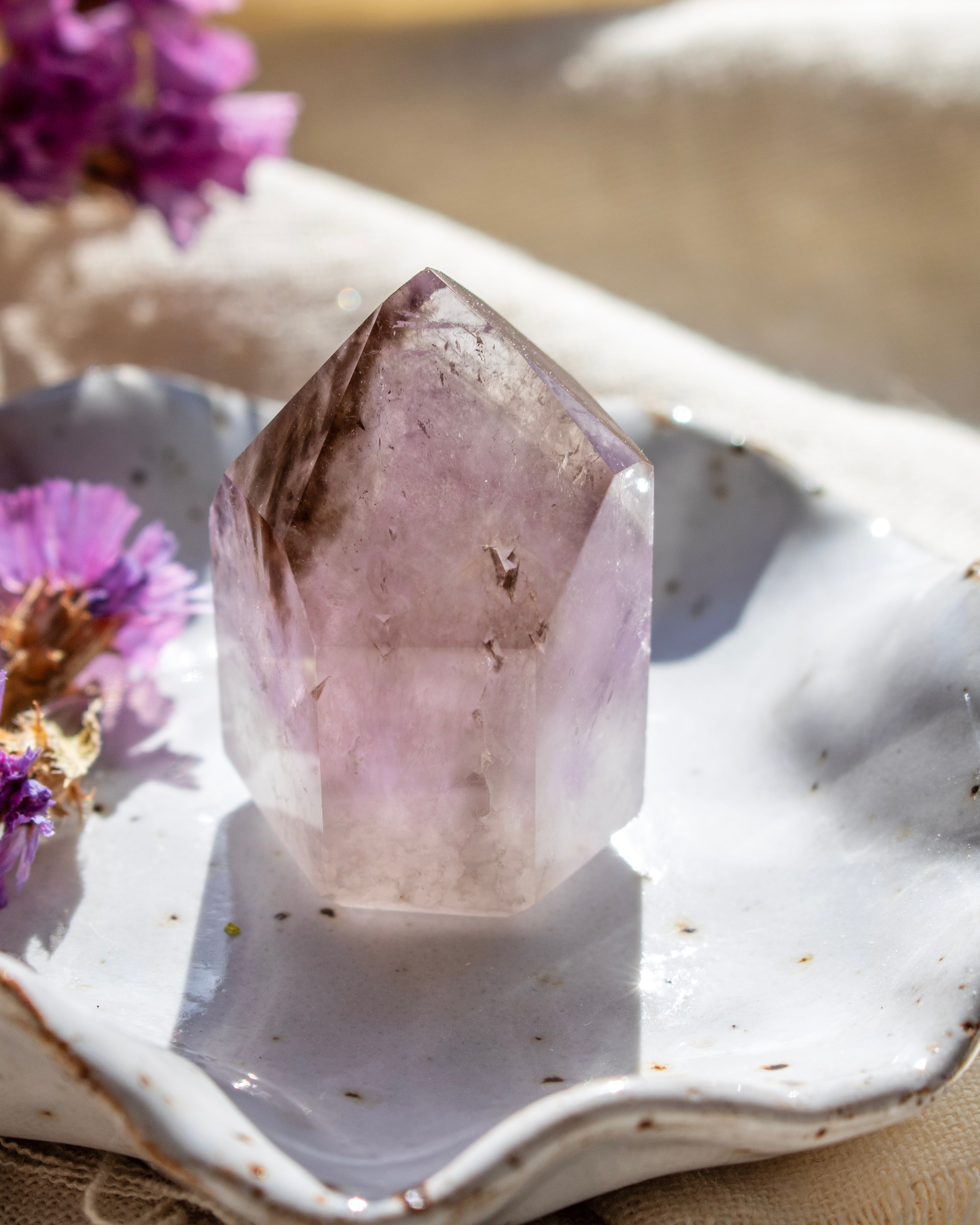 Amethyst crystal on a white ceramic dish with purple flowers.