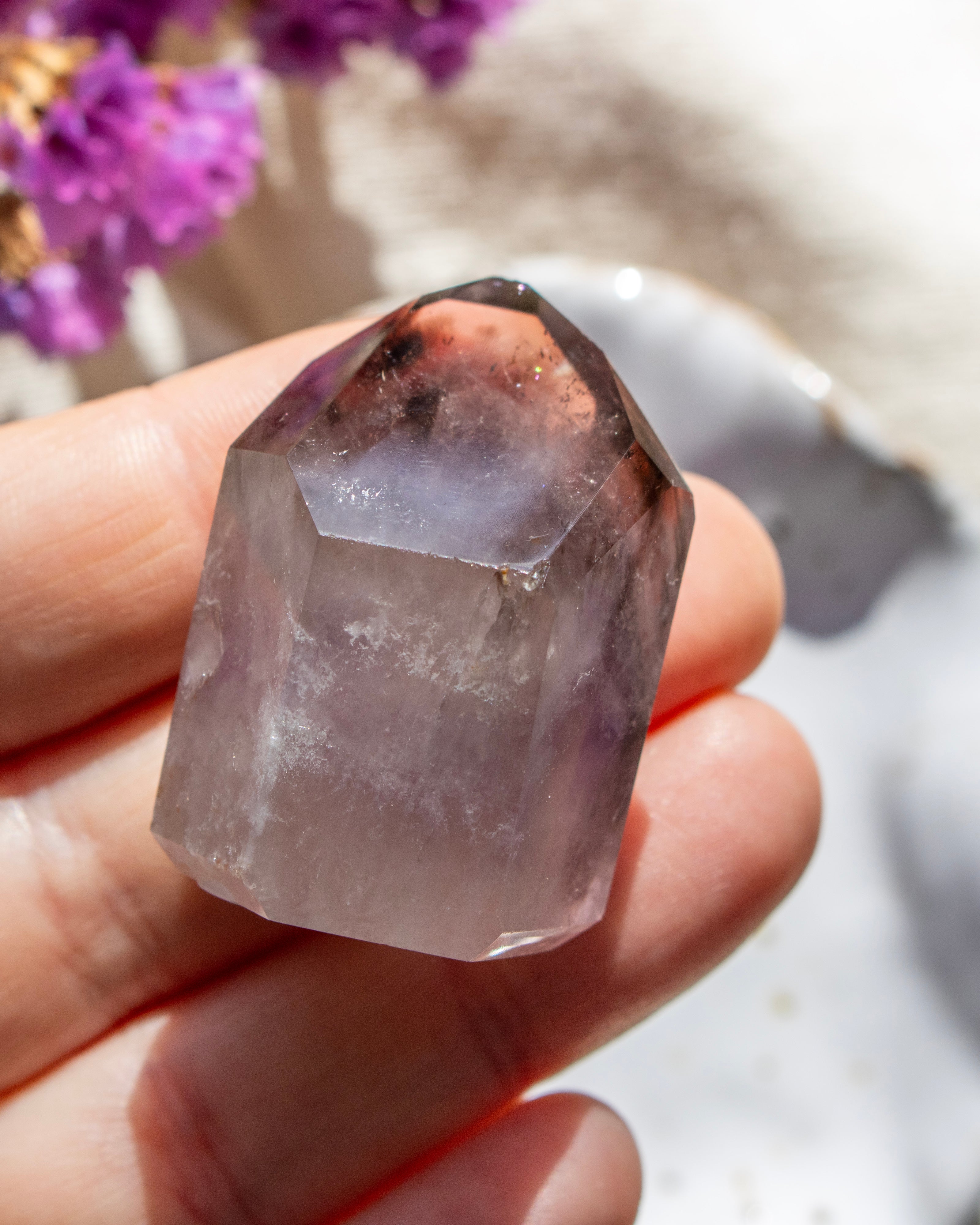 Hand holding a clear crystal with purple undertones against a blurred natural background