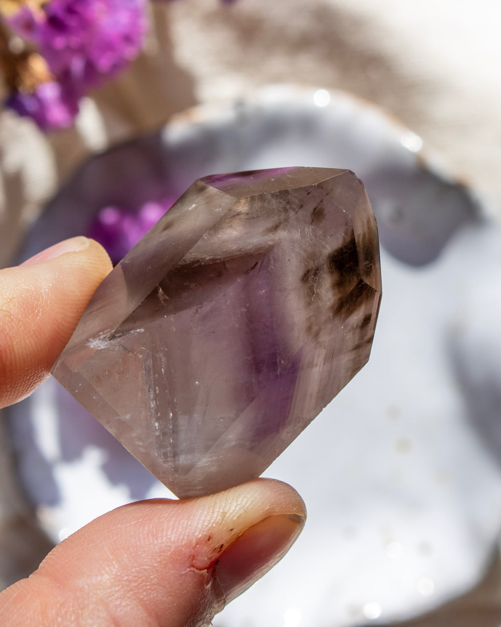 Hand holding a purple crystal with a blurred natural background