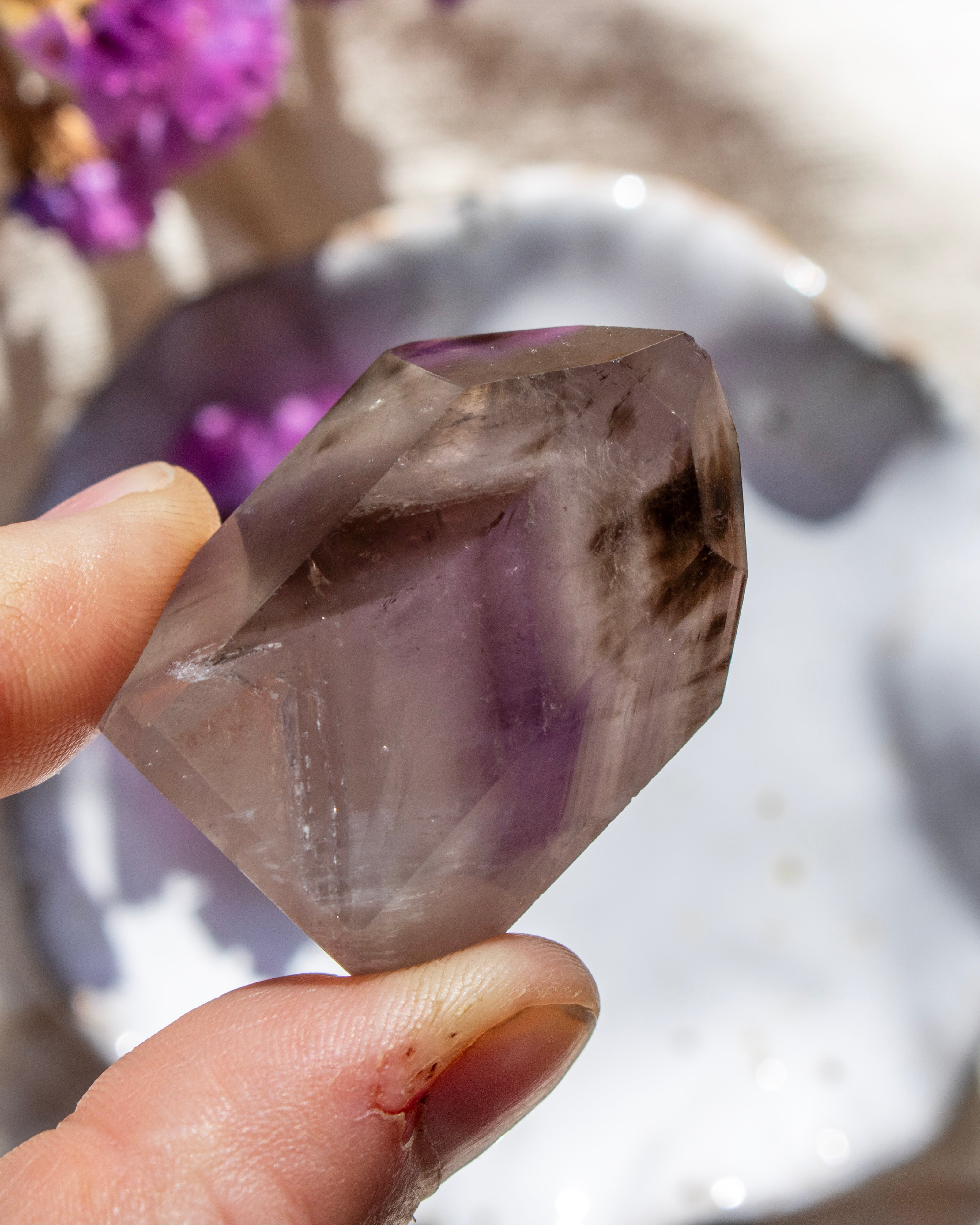 Hand holding a purple crystal with a blurred natural background