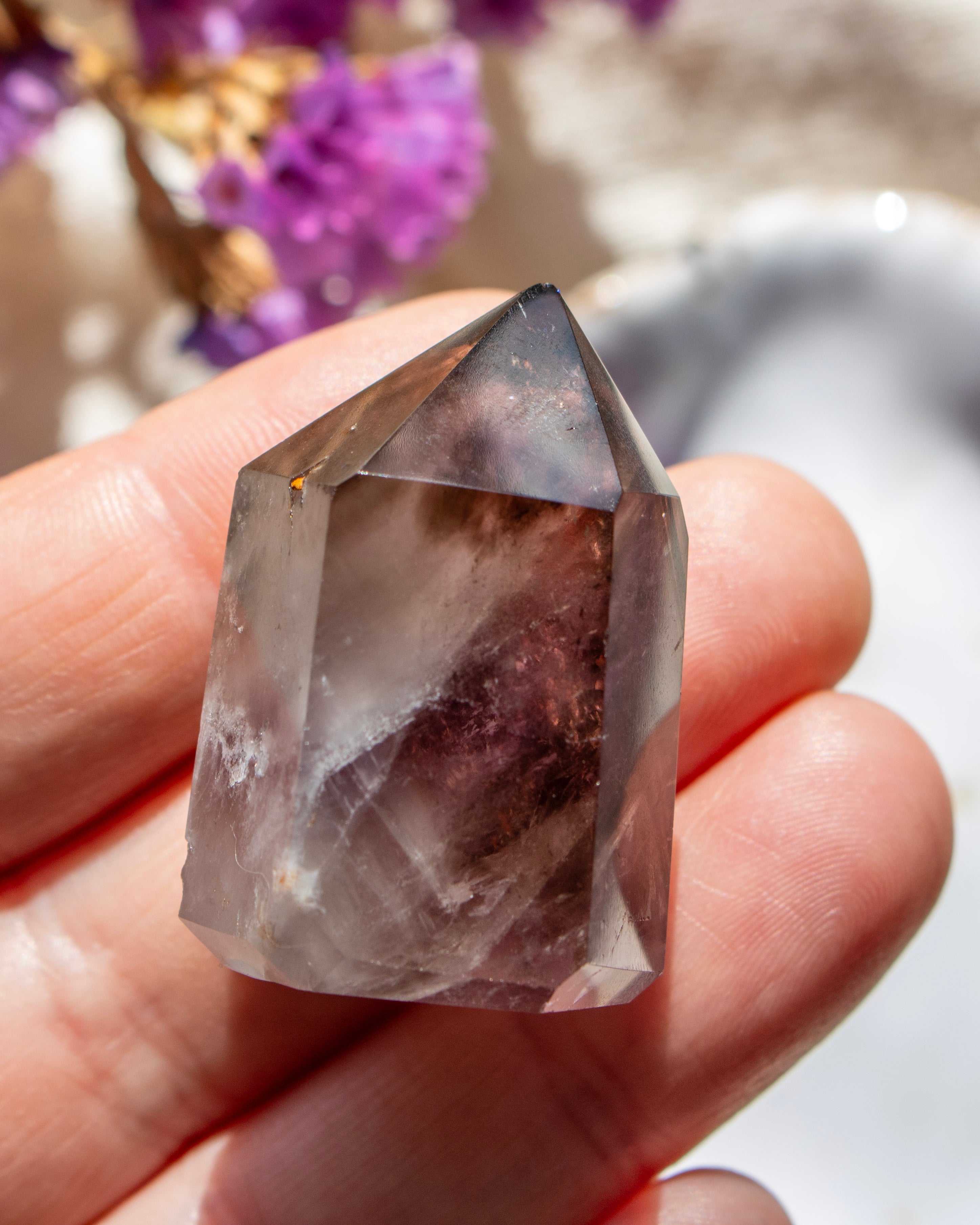 Crystal held in a hand with blurred purple flowers in the background