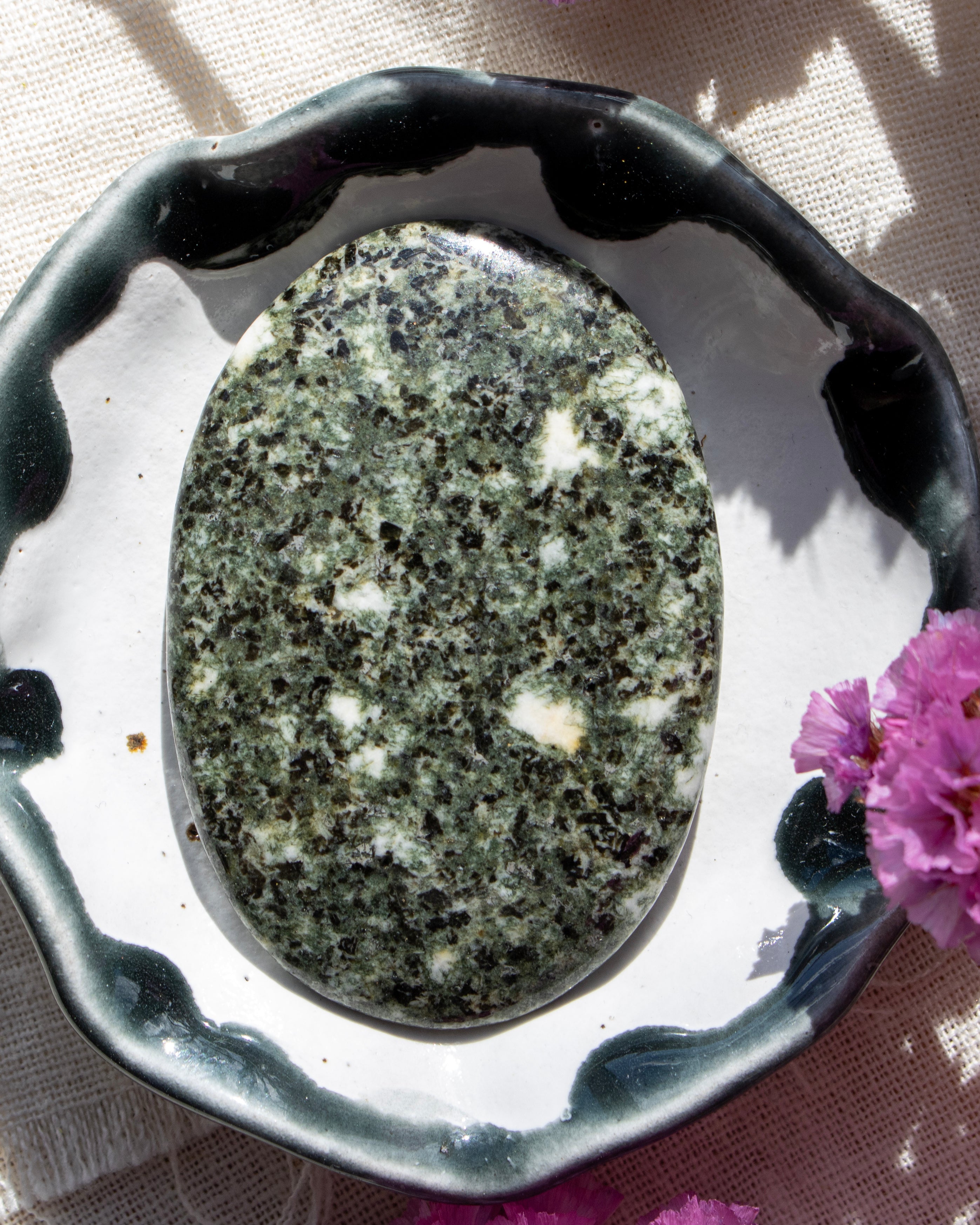 Green stone in a decorative holder with a pink flower on a light background