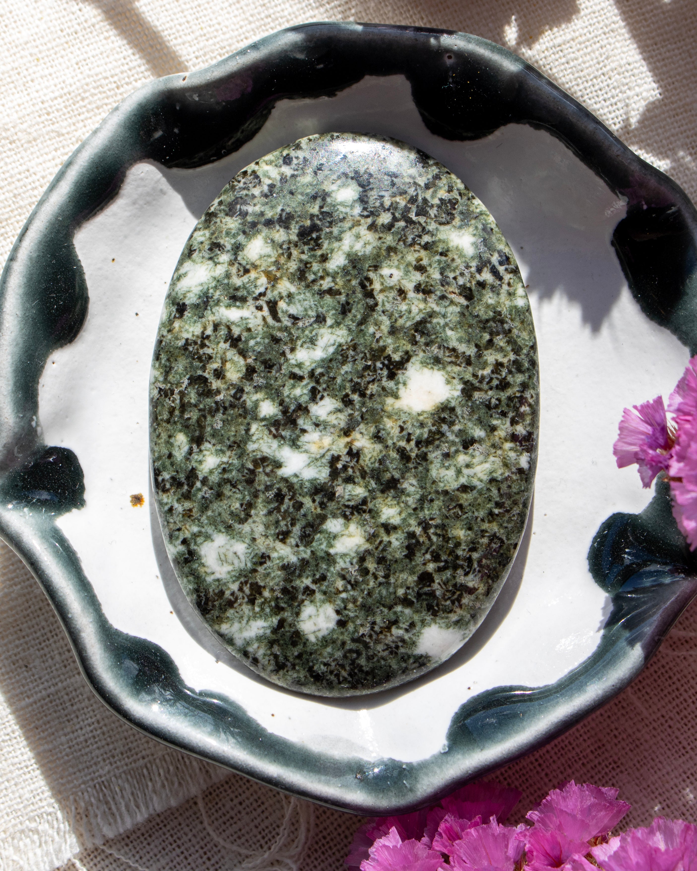Oval-shaped stone on a decorative stand with pink flowers in the background