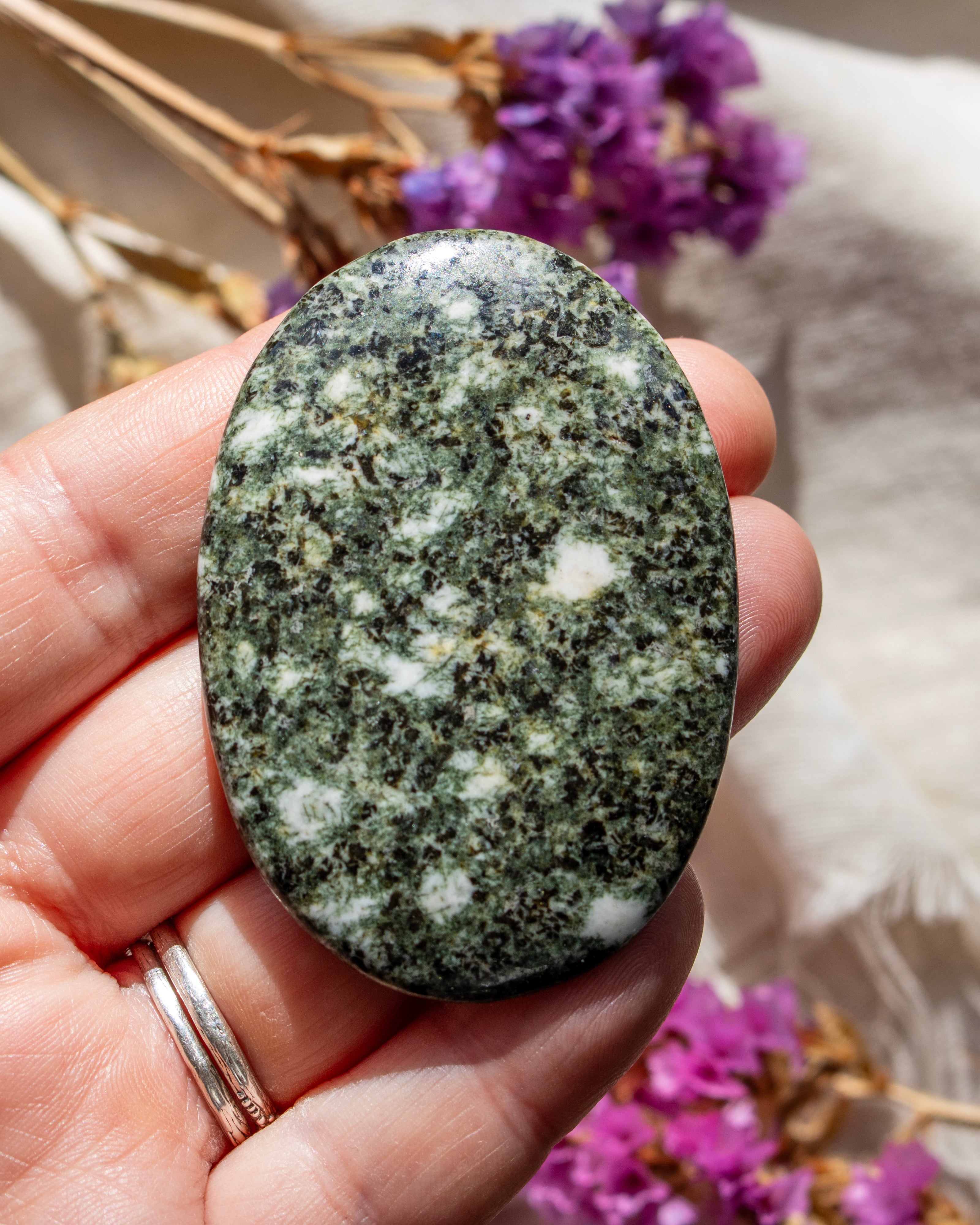 Oval-shaped green stone held in a hand with blurred purple flowers in the background