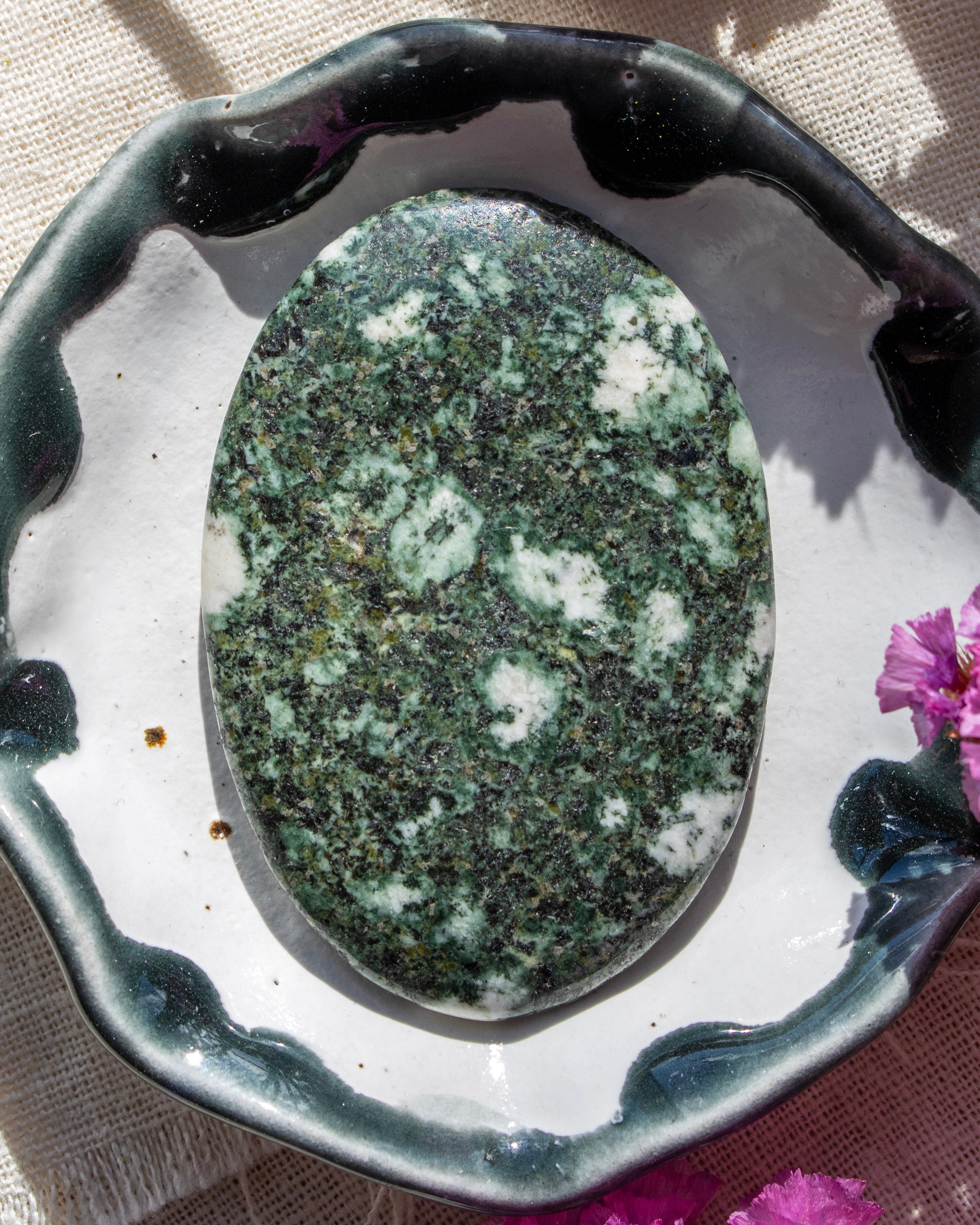 Green and white speckled stone on a decorative stand with pink flowers in the background