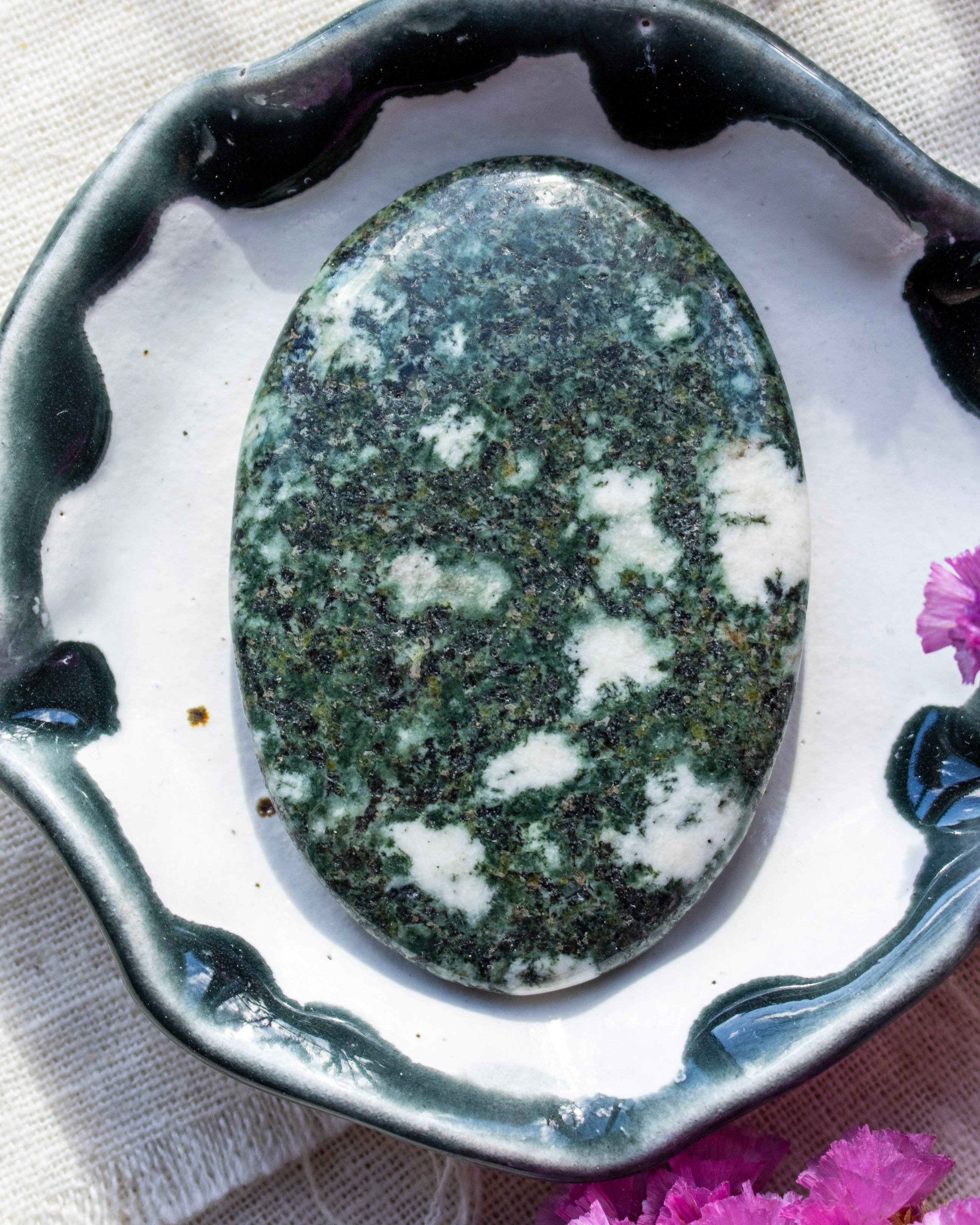 Oval-shaped green and white stone on a decorative black and white dish with pink flowers.
