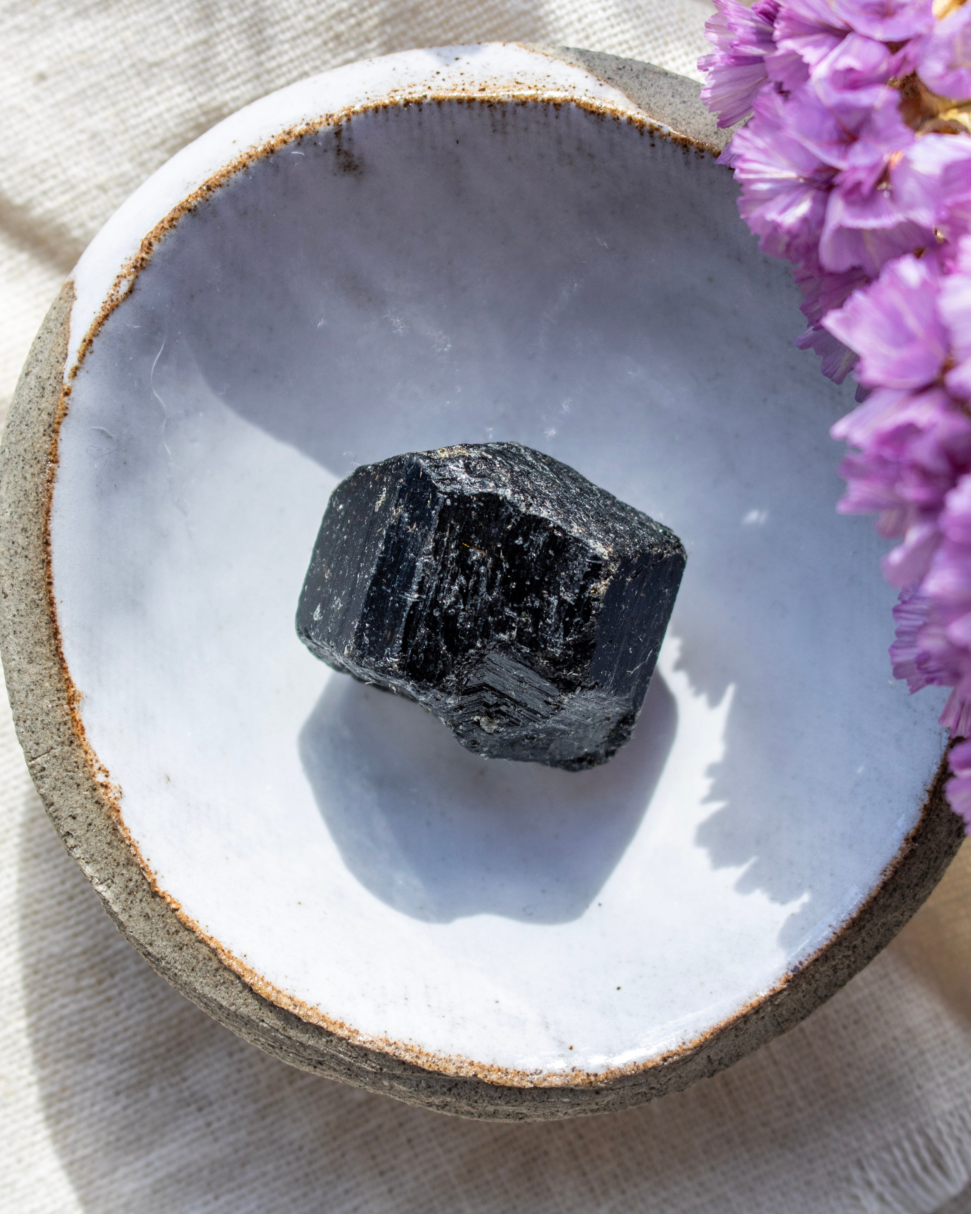 Black stone in a ceramic dish with purple flowers on a light fabric background