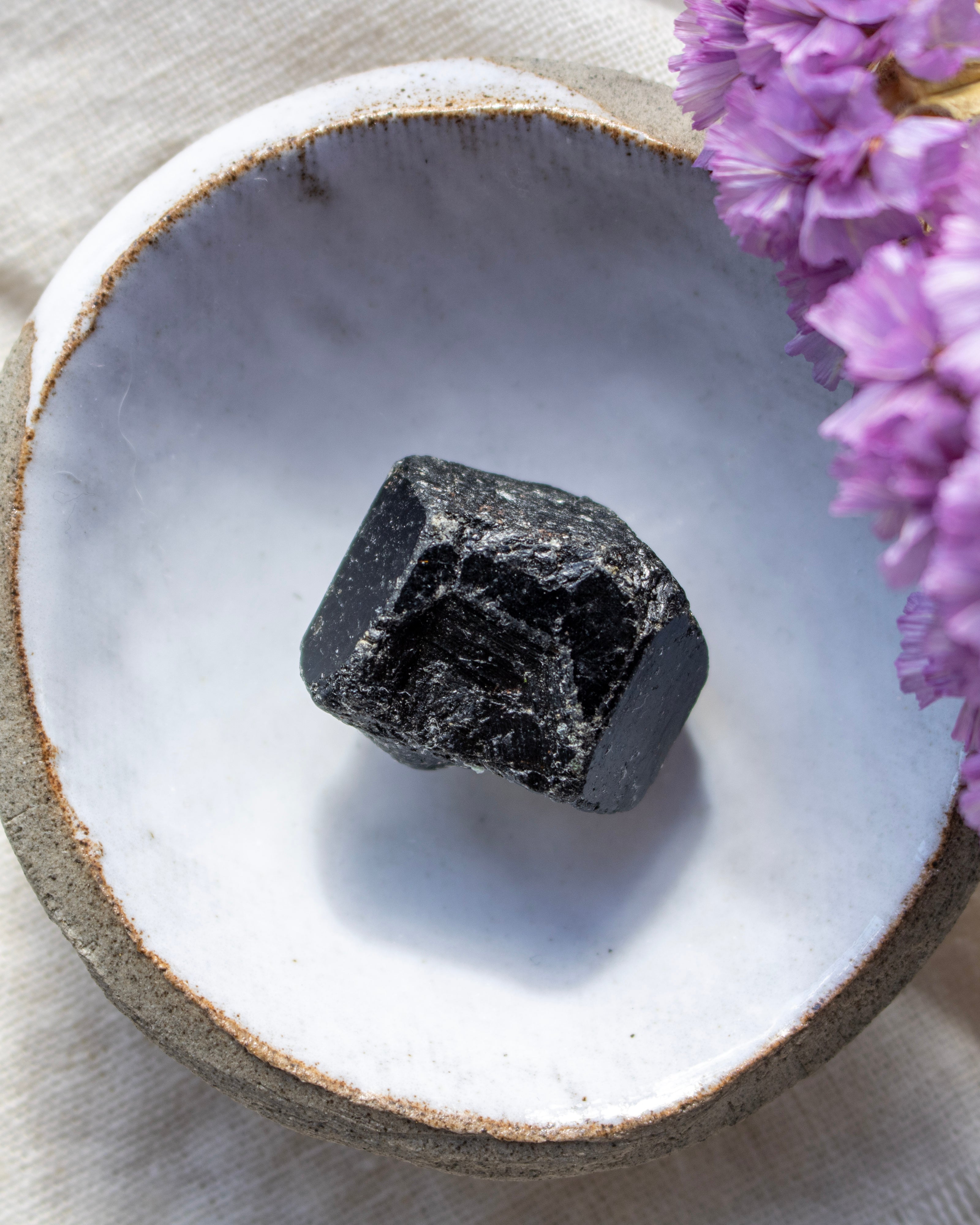 Black crystal on a white ceramic dish with purple flowers in the background