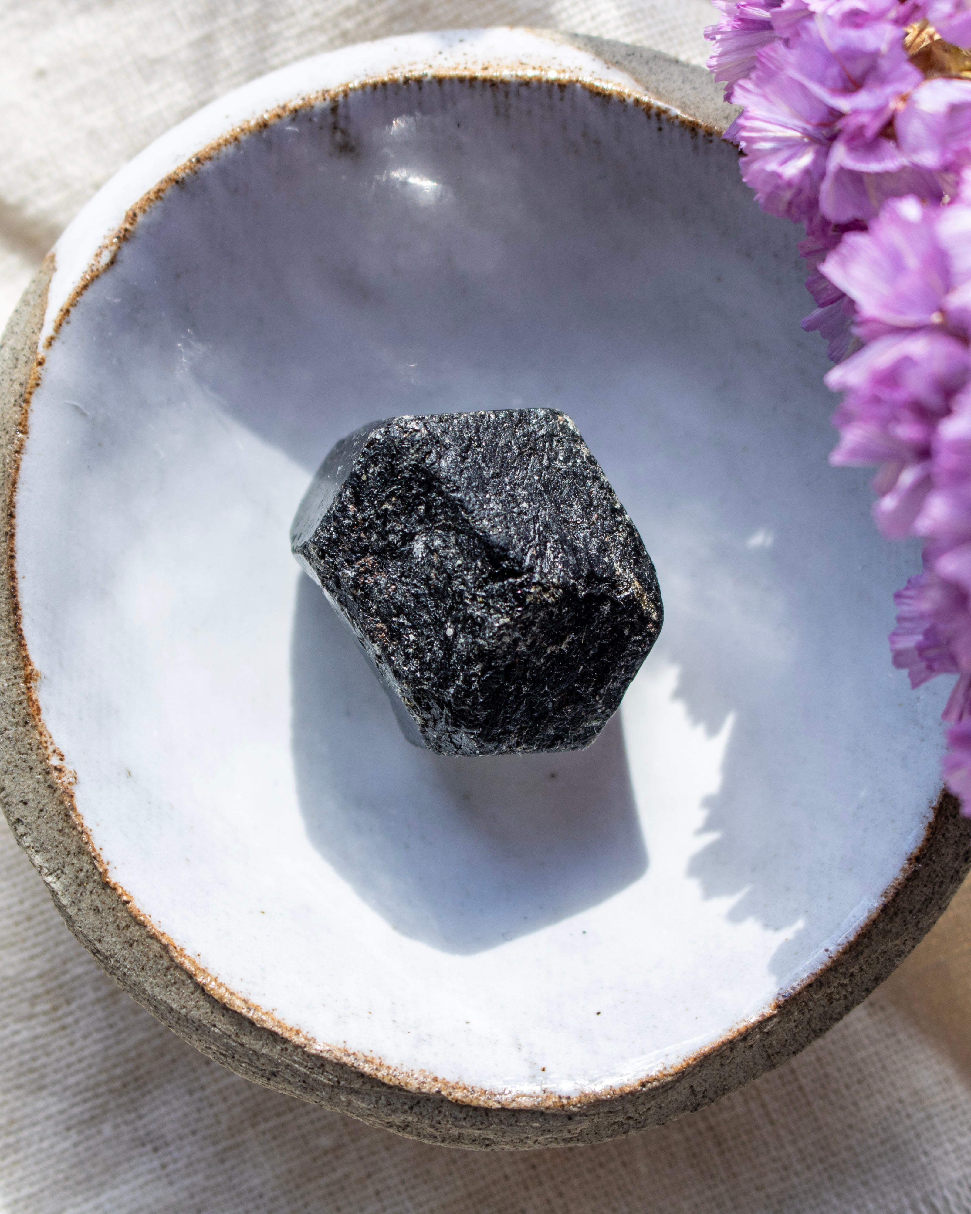 Black crystal on a white ceramic dish with purple flowers in the background