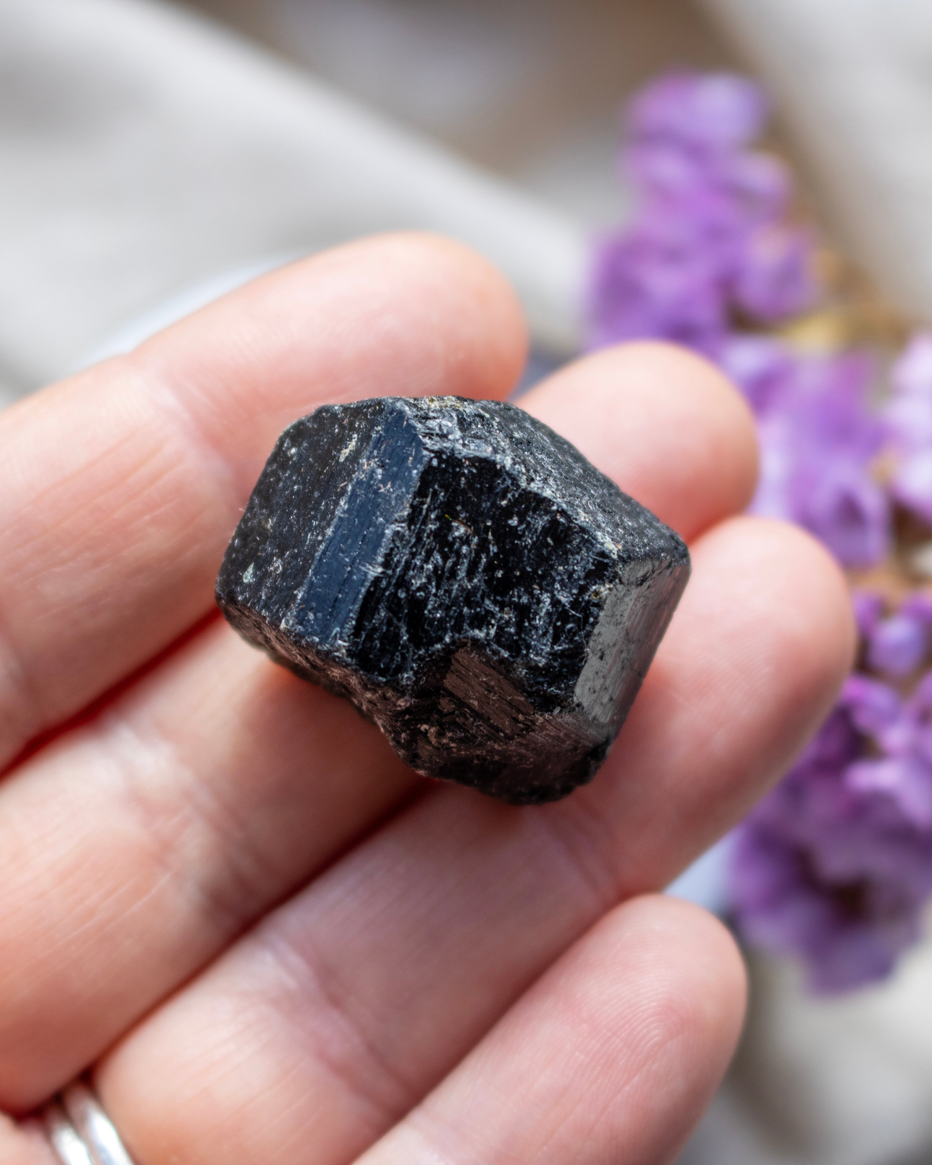 Black crystal held in a hand with blurred purple flowers in the background