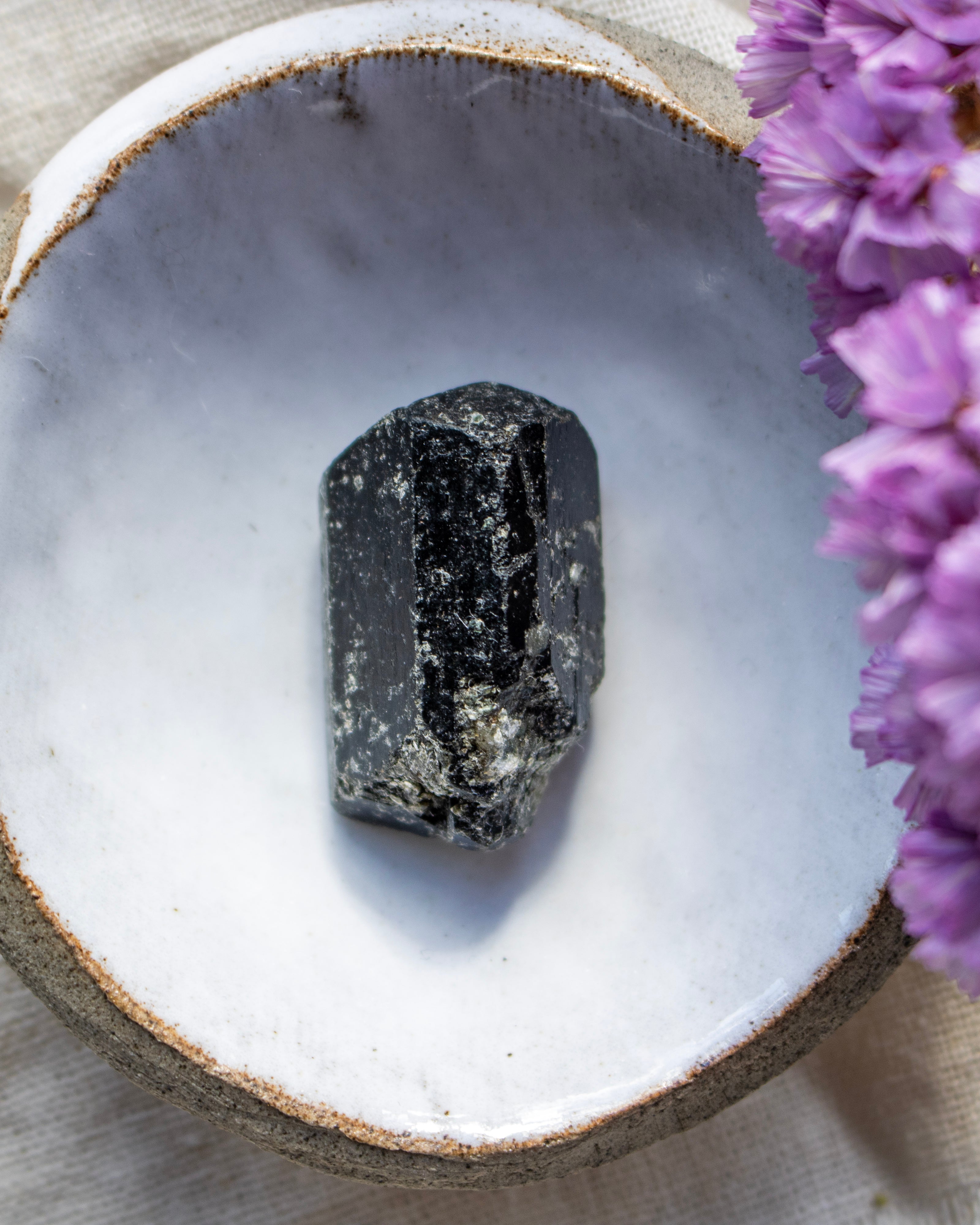 Black crystal on a white stone surface with purple flowers