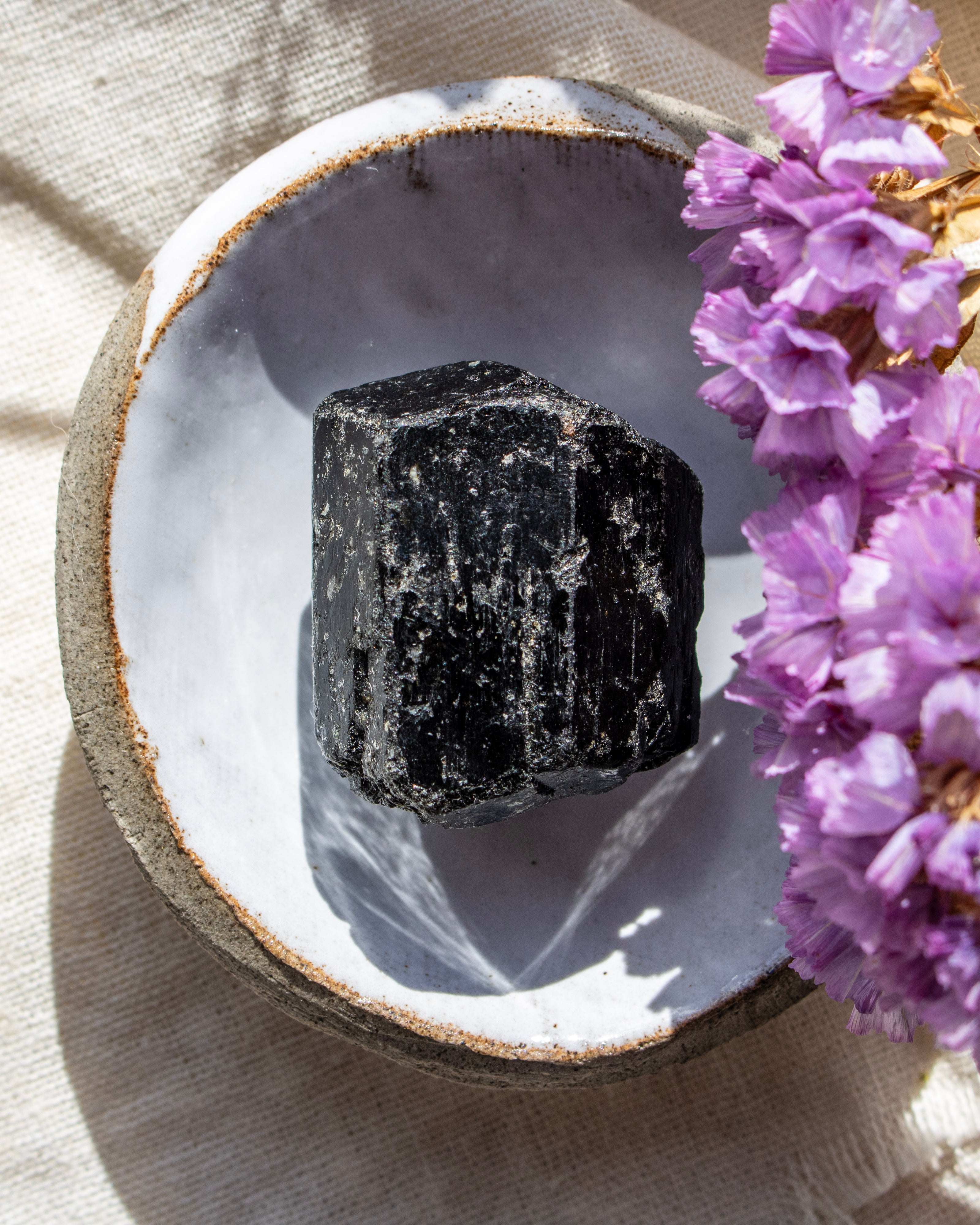 Black crystal on a white stone surface with purple flowers